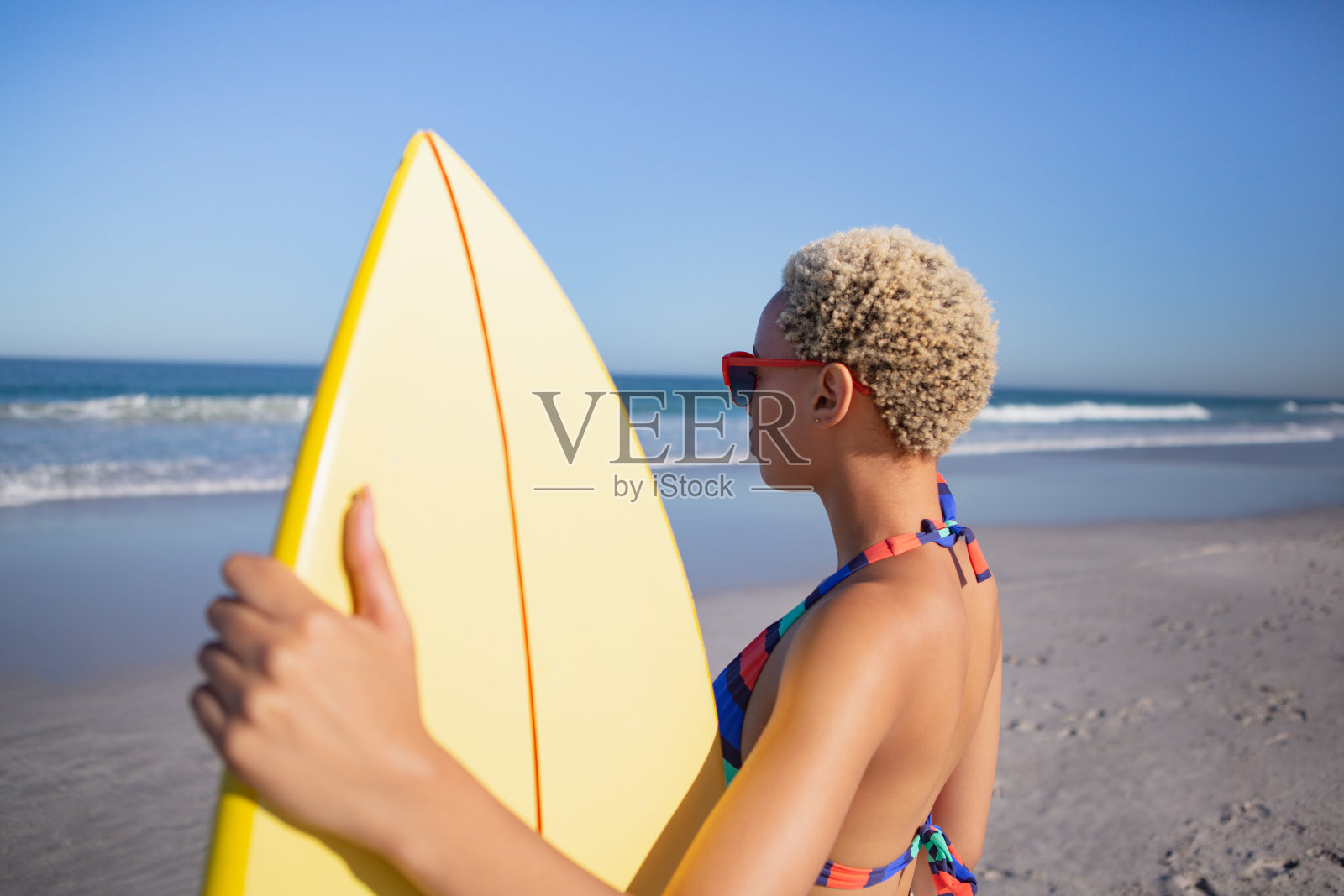 美丽的女人穿着比基尼和太阳镜站在海滩冲浪板在阳光下照片摄影图片