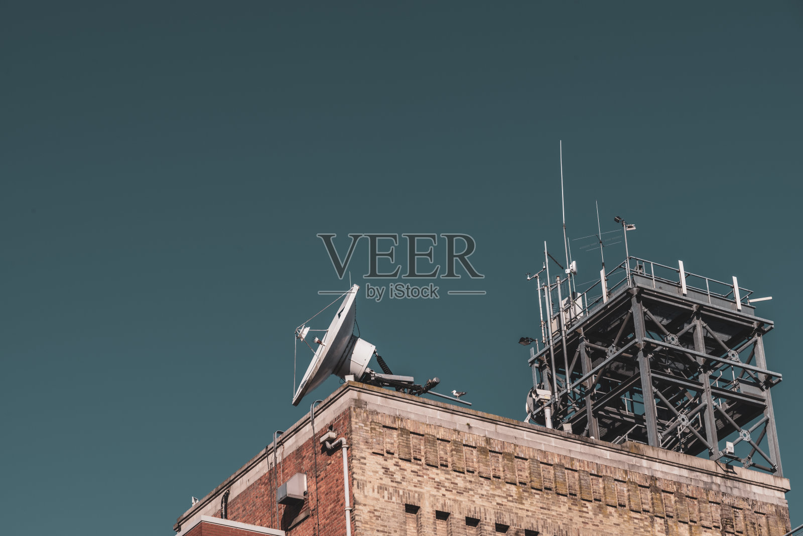 卫星盘和通讯塔位于一座砖砌建筑的屋顶上照片摄影图片