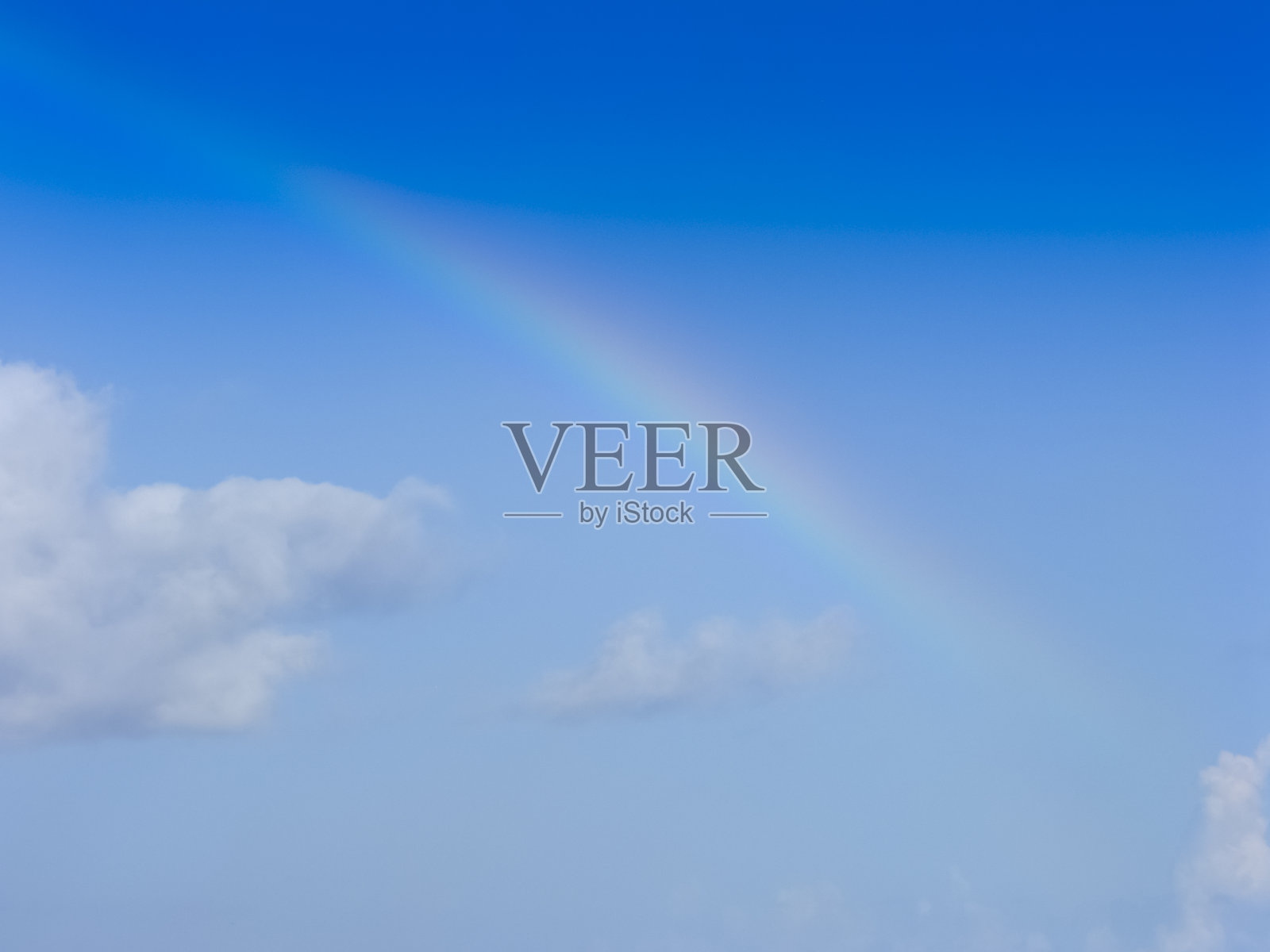 在蓝色的天空和小白云微弱的彩虹-开始和结束彩虹在中间拍摄-非常轻的彩虹在蓝色背景照片摄影图片