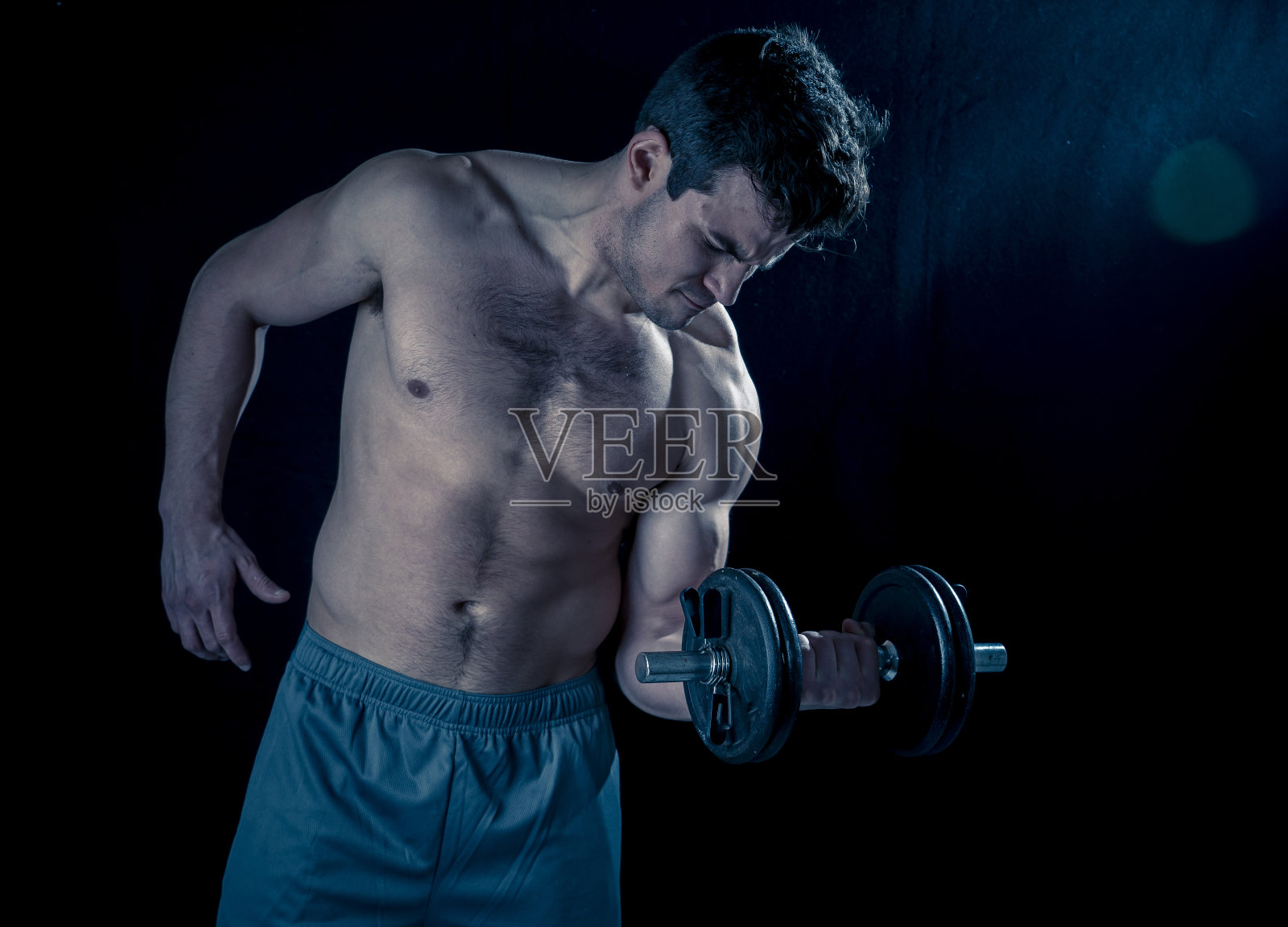 肖像年轻肌肉发达的运动员男子工作做练习和摆姿势与哑铃，健美男性举重在健身运动身体护理和健康的生活方式。照片摄影图片