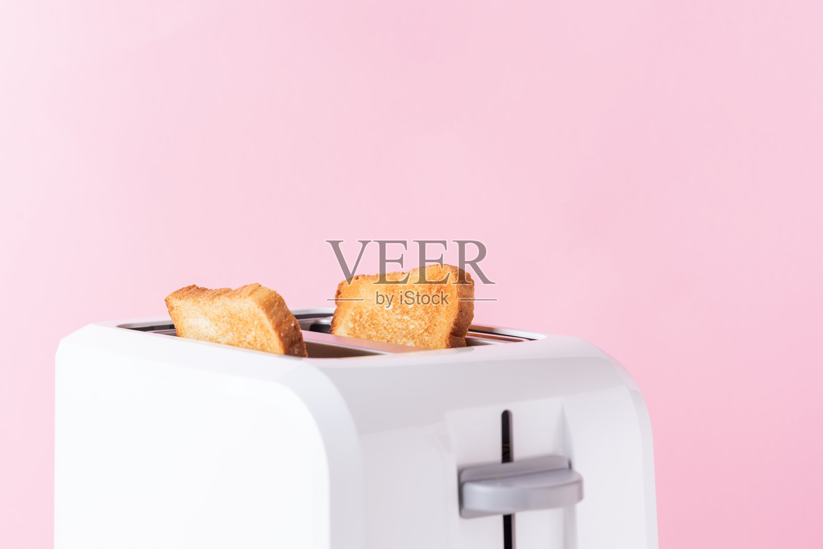 白色烤面包机与烤面包在粉红色的背景，近照片摄影图片