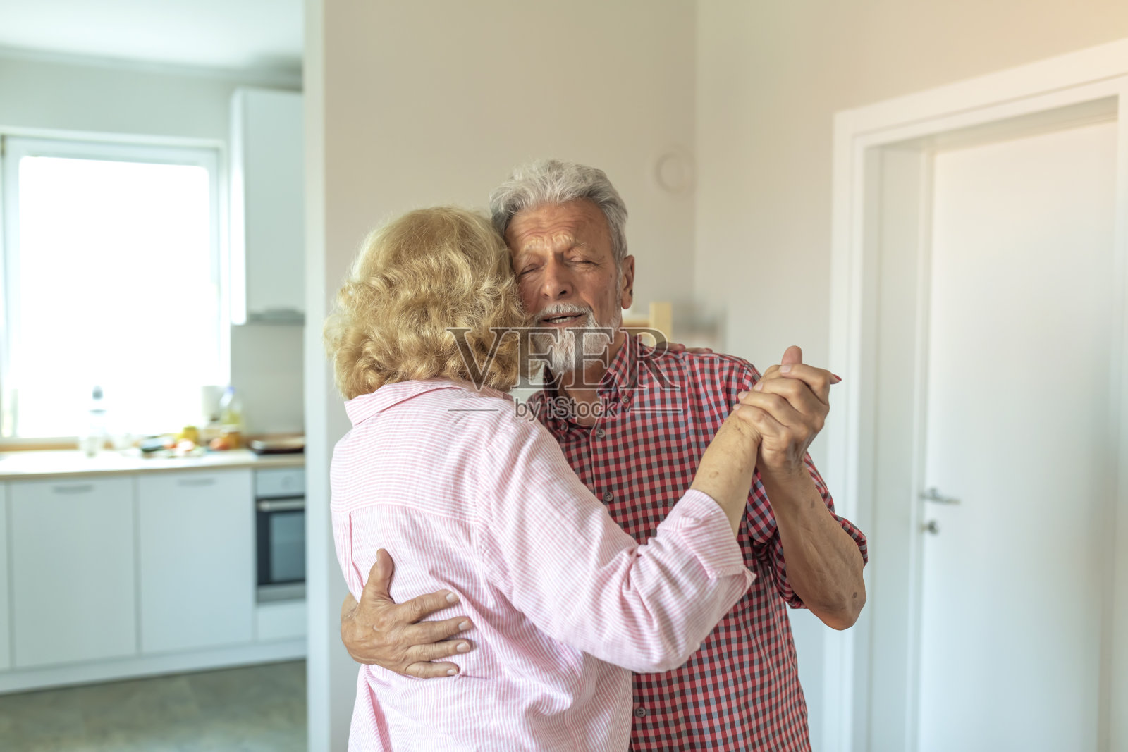 快乐的老夫妇跳着华尔兹，微笑着。快乐的老年夫妻在家里跳舞。照片摄影图片