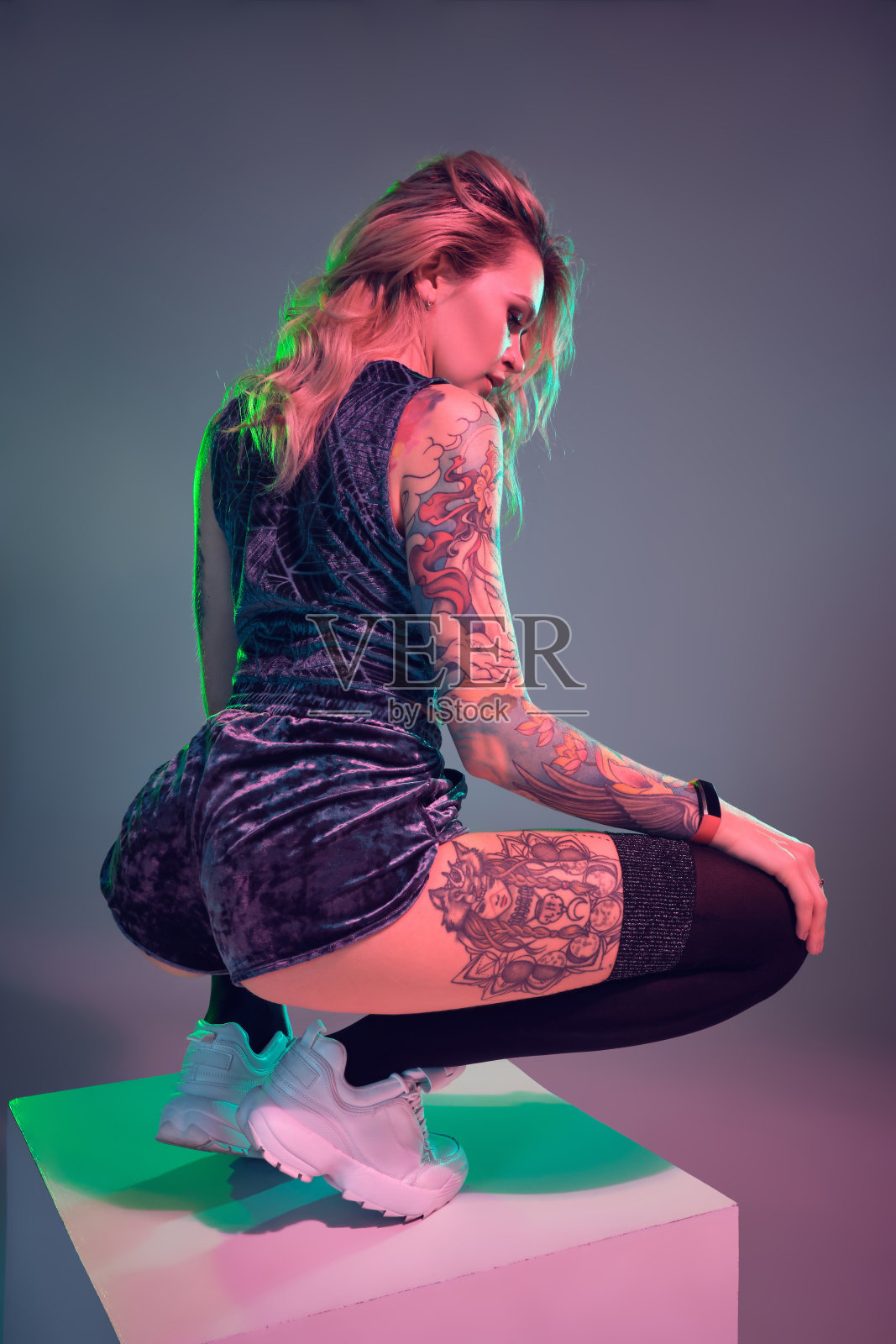 年轻的健身金发女人穿着蓝色天鹅绒短靴在镜头前摆姿势，蹲在一个大的立方体上照片摄影图片