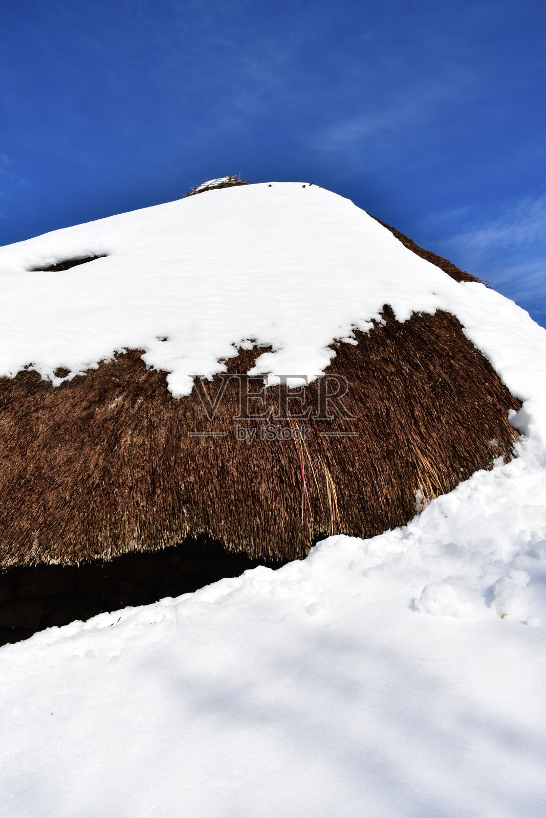 用石头和稻草建造的古老积雪的palloza房子。屋顶特写被雪覆盖。西班牙卢戈，皮奥内多的蓝天。照片摄影图片