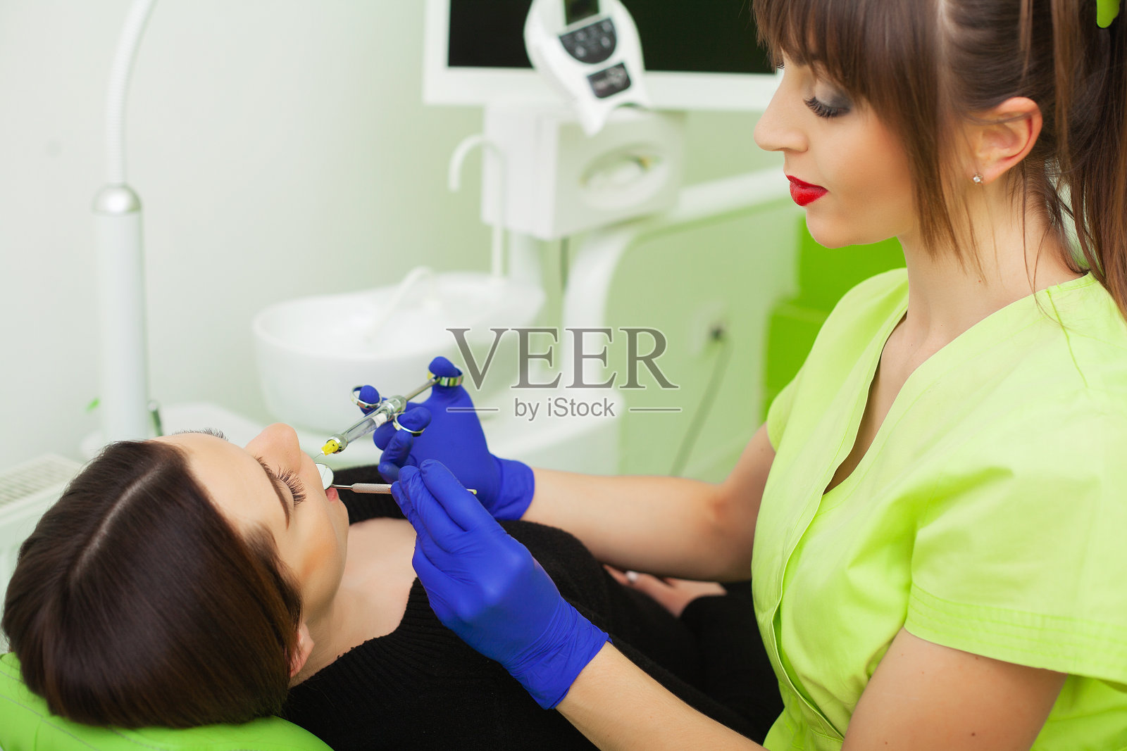 牙医手里拿着工具和注射器。止痛剂在起作用。女病人张着嘴。美丽的微笑和洁白的牙齿照片摄影图片