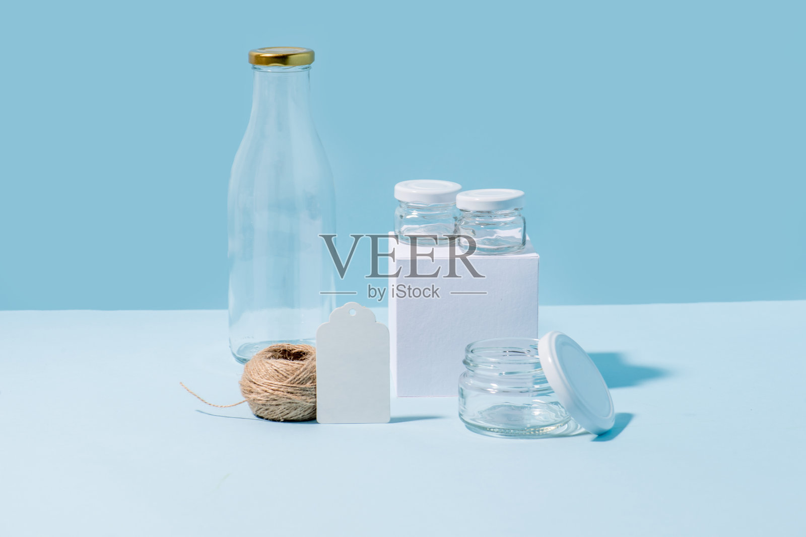 蓝色背景上有一捆麻绳的玻璃瓶和罐子。照片摄影图片