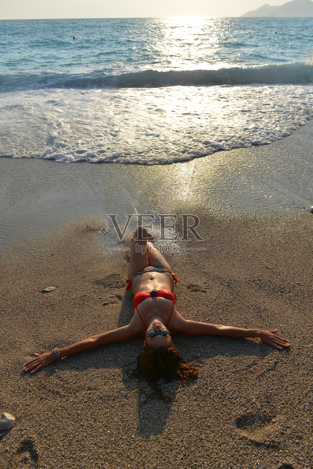 女人有乐趣躺在海浪在日落的大海。照片摄影图片