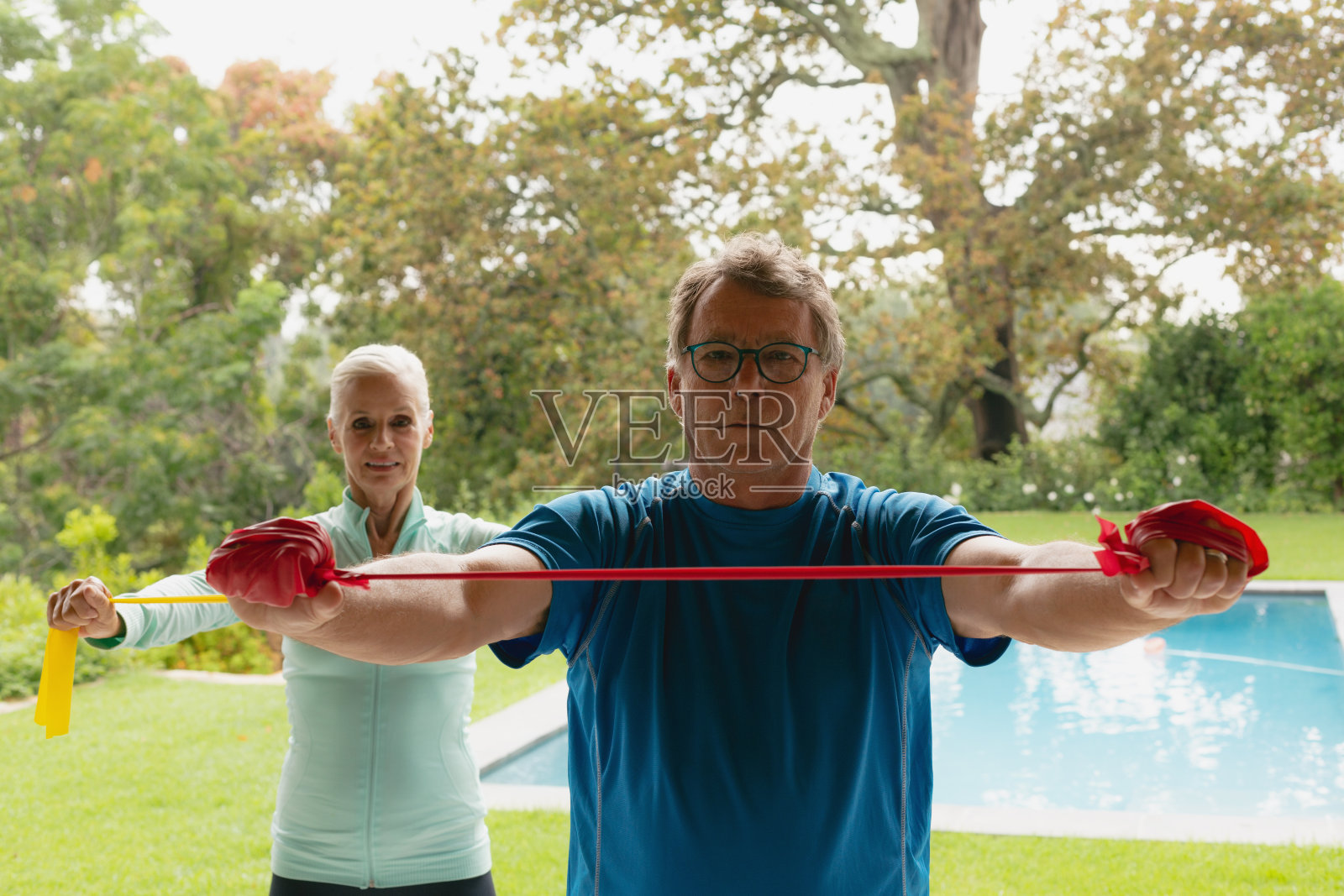 一对活跃的老年夫妇在家里的门廊上和抵抗乐队一起锻炼照片摄影图片