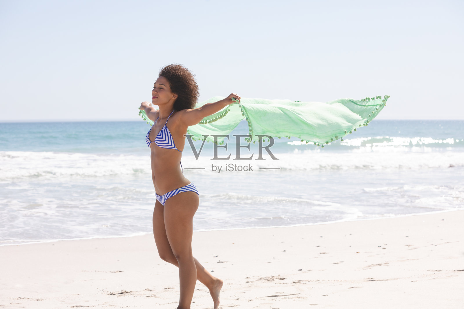 穿着比基尼、围着围巾的女人站在沙滩上照片摄影图片