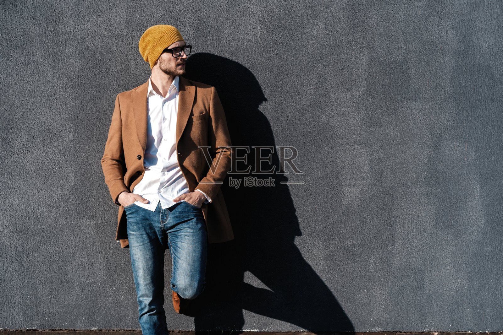 一幅帅气的胡须男子的肖像，穿着时髦的衣服，站在街道上，以灰色的墙壁为背景照片摄影图片