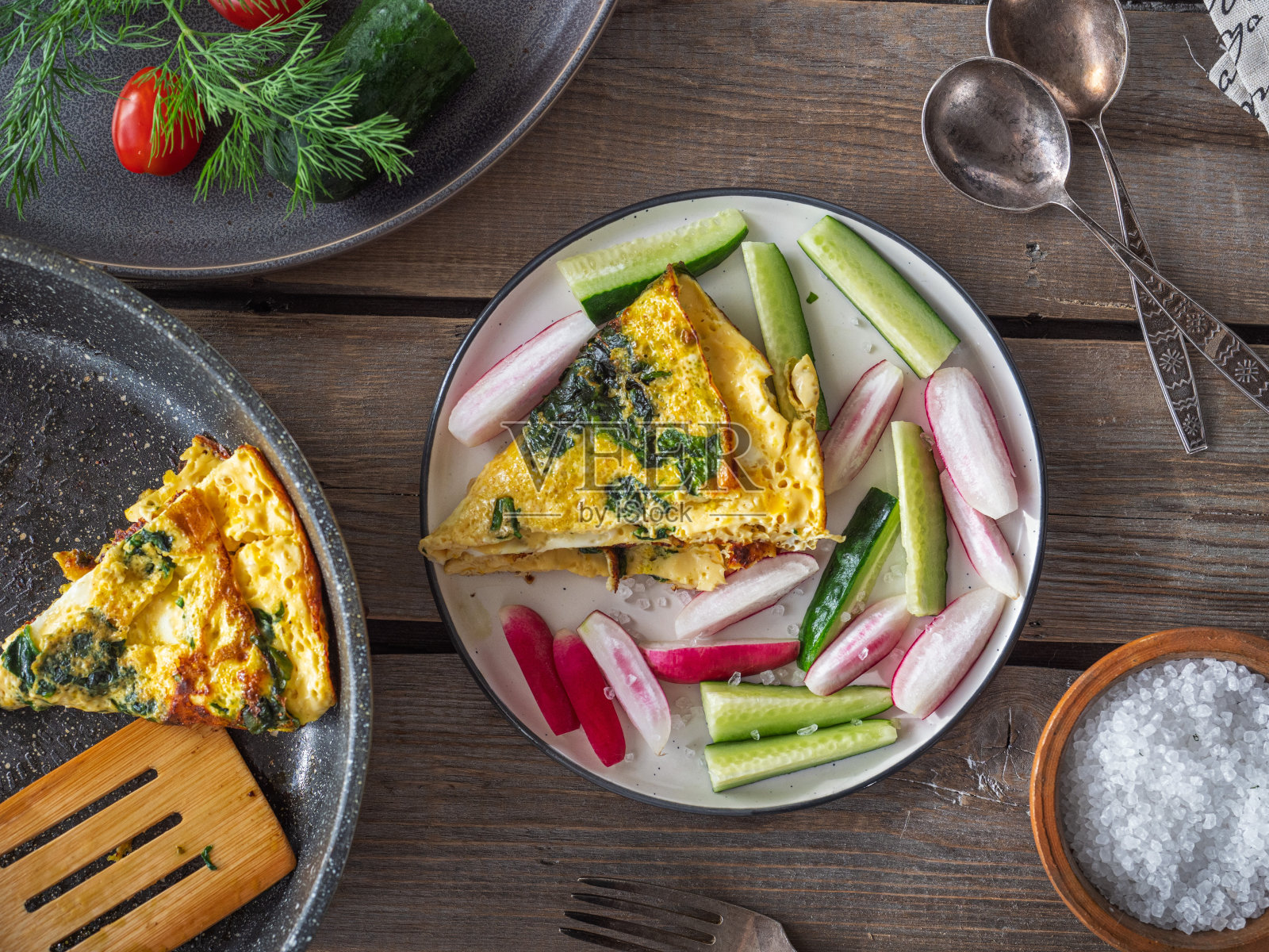 早餐是菠菜炒蛋和切好的蔬菜，整棵的蔬菜和一个煎锅，煎蛋片和刀叉放在粗糙的木板桌上，从顶部取下照片摄影图片