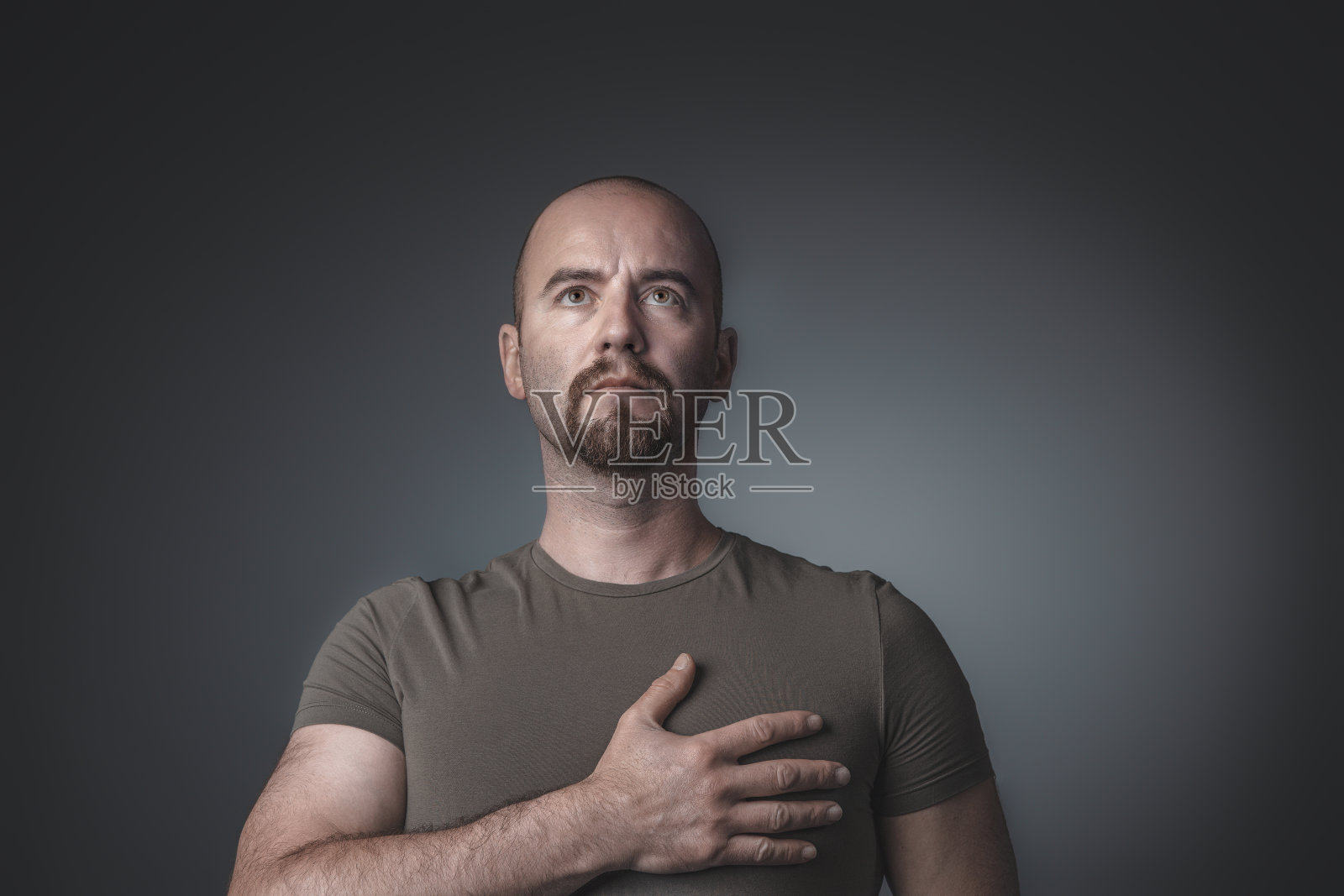 一个男人抬起头，把一只手放在心脏上方的肖像。照片摄影图片