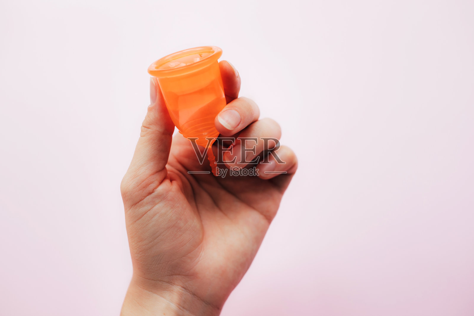 粉红色背景上，女士手握月经杯。照片摄影图片