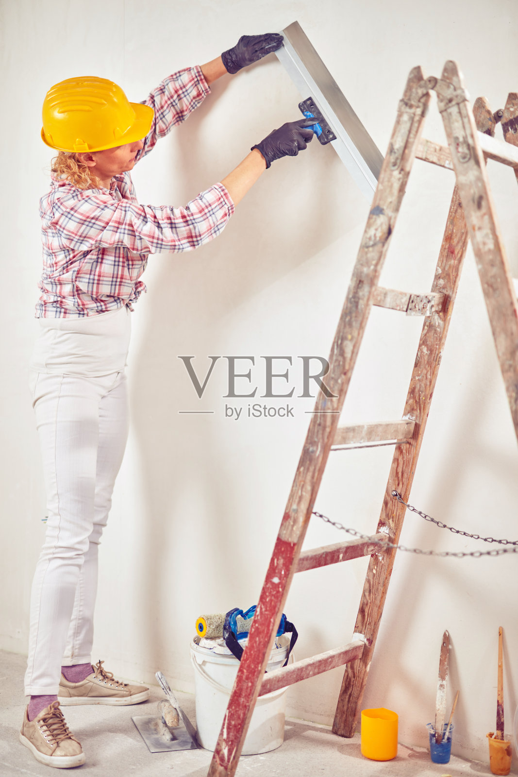 在房子内部粉刷墙壁的女工。照片摄影图片