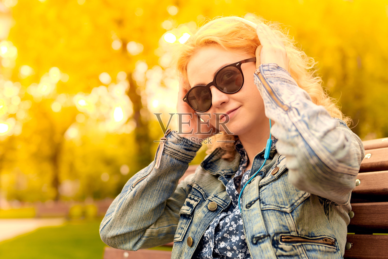 年轻的金发女子戴着耳机坐在公园的长椅上听音乐，表达着快乐和幸福的情感照片摄影图片