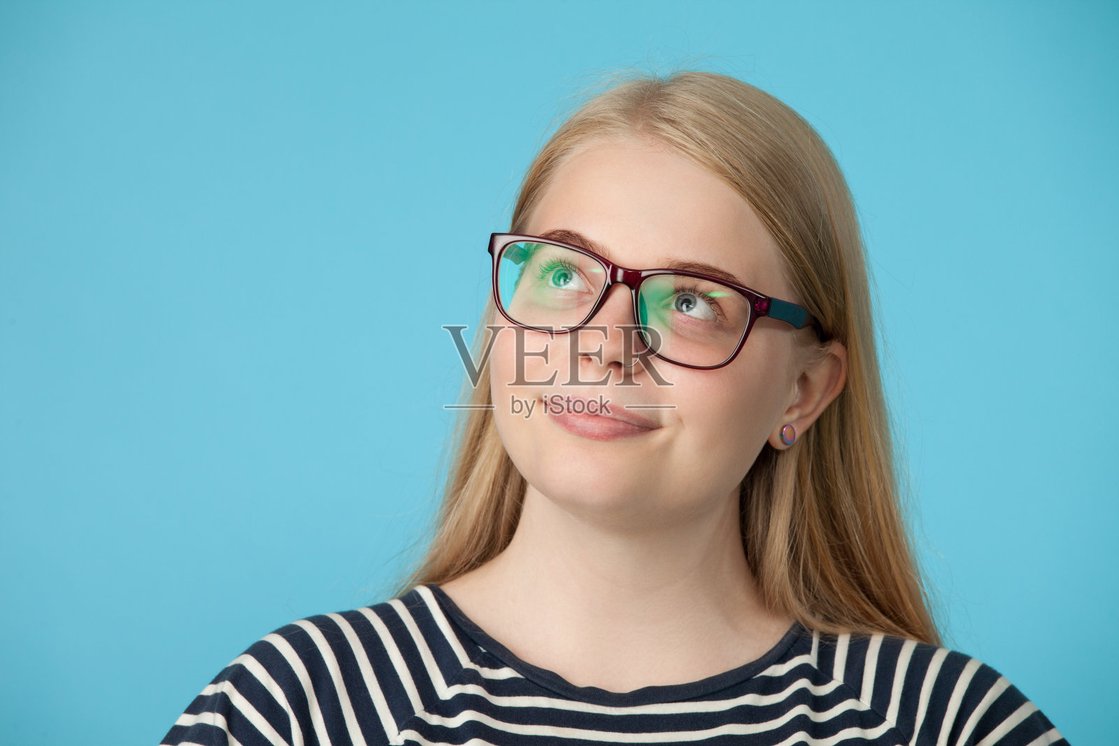 一个迷人的20岁金发女人的工作室肖像与眼镜上的蓝色背景照片摄影图片