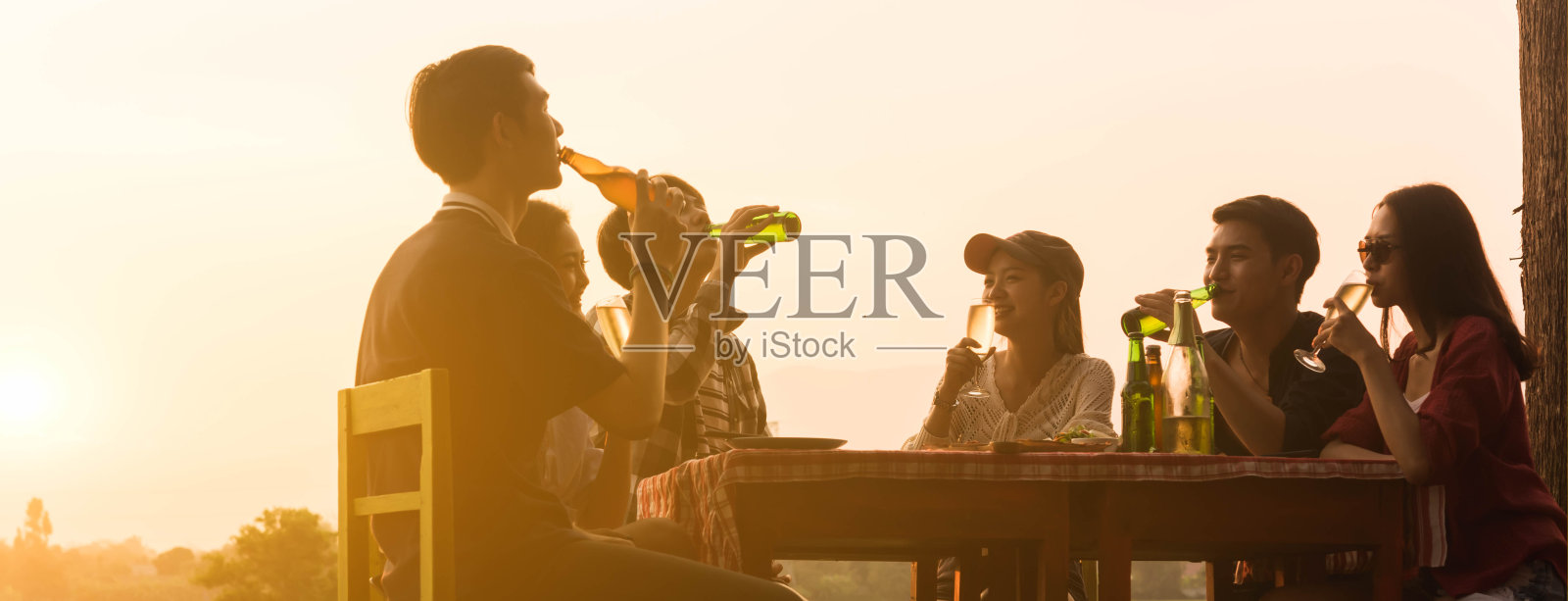 在美丽的风景背景下，6名青少年在日落时举行晚宴庆祝，为横幅裁剪了尺寸照片摄影图片