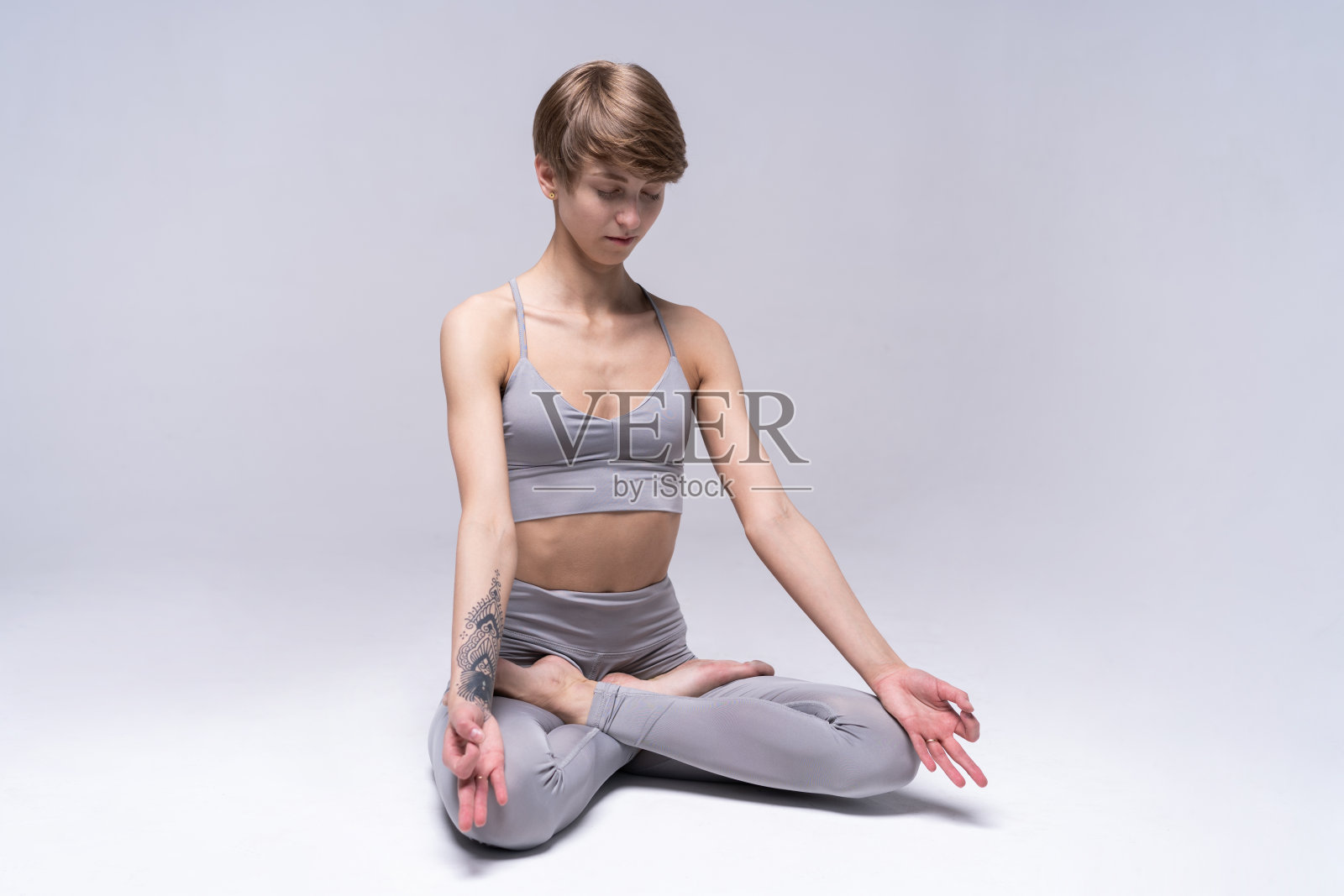 年轻迷人的微笑女子练习瑜伽，坐在半莲花运动，阿达莲花姿势，锻炼，穿着运动服。照片摄影图片