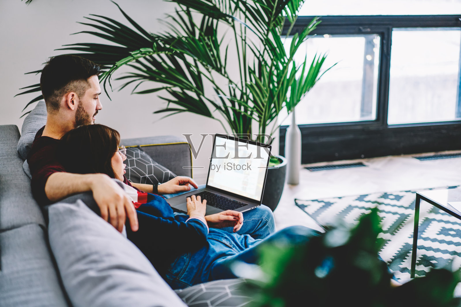 丈夫拥抱年轻的妻子和网上订票的现代笔记本电脑上的空间使用无线互联网和享受家的舒适。在公寓里用电脑看电影照片摄影图片