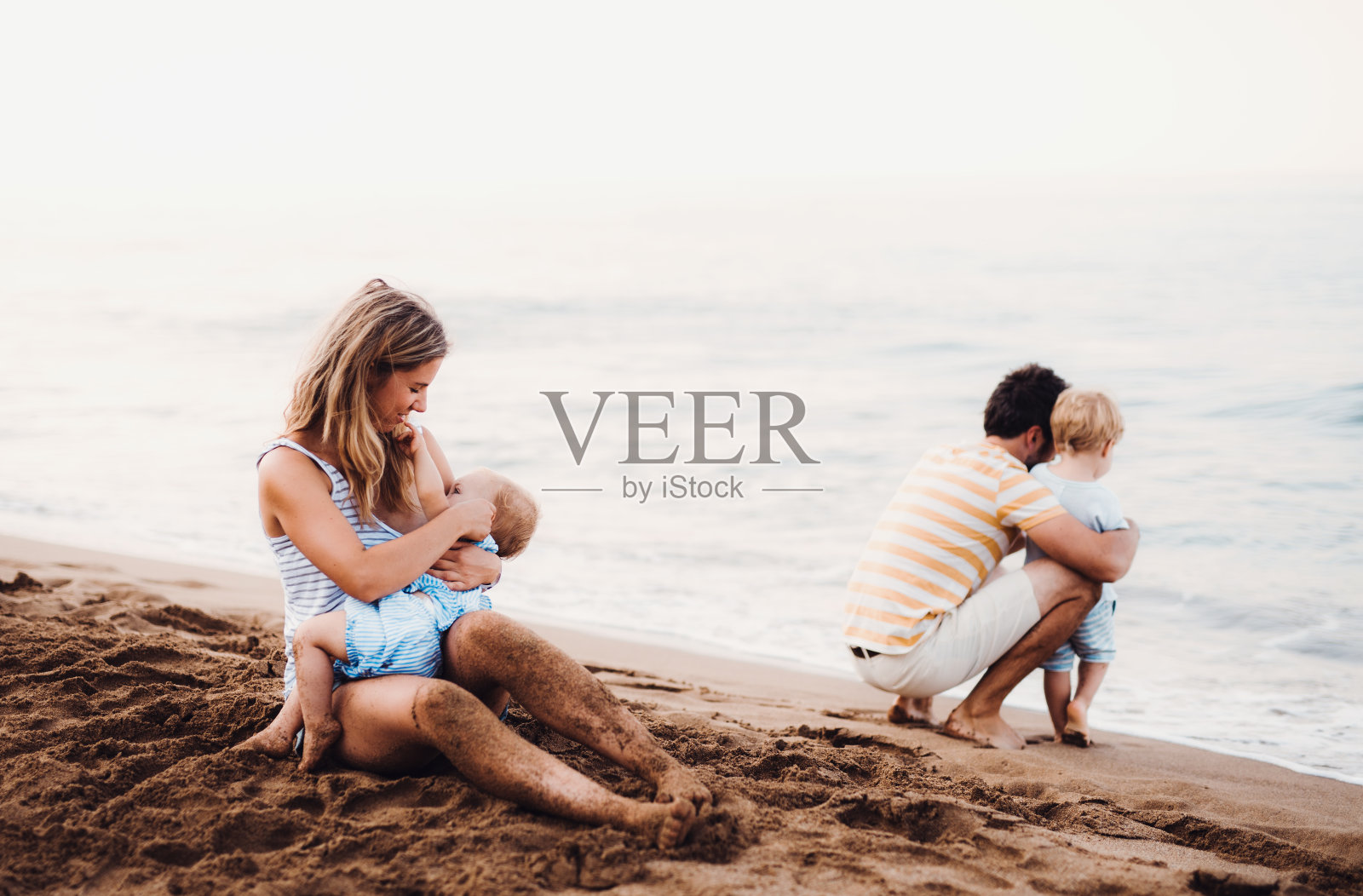 一个年轻的家庭带着两个蹒跚学步的孩子在海滩上度假。照片摄影图片