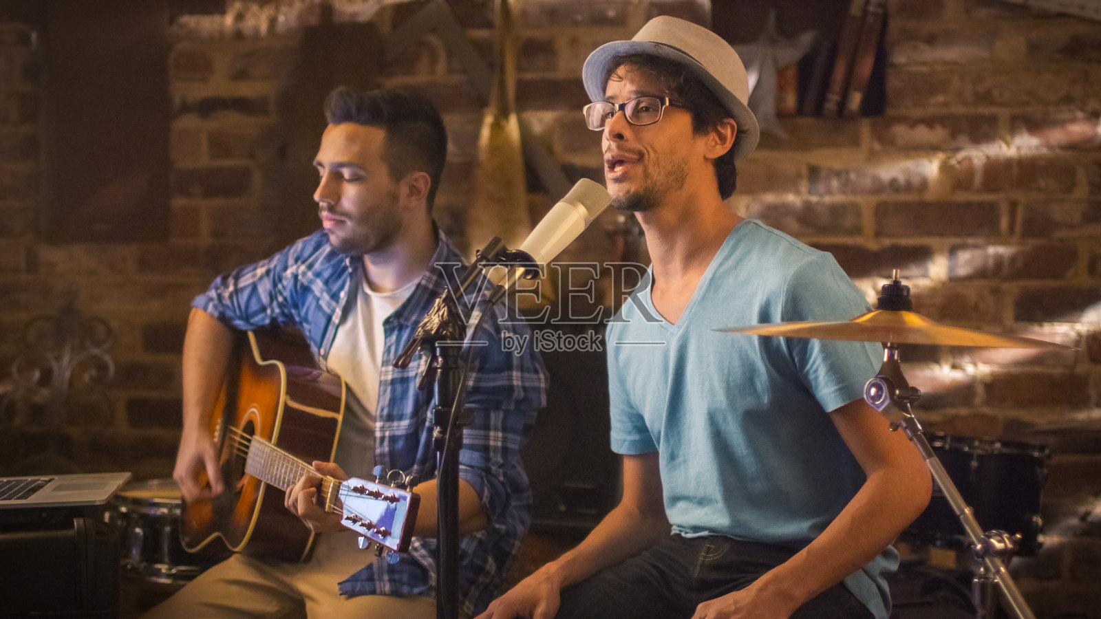 两个年轻人边唱边弹吉他，在车库的家庭录音室里录制了一首歌。照片摄影图片