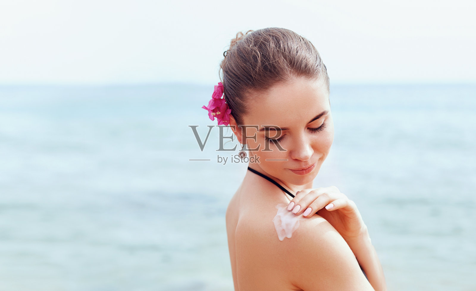 女人在晒黑的肩膀上涂防晒霜。护肤品。身体防晒防晒霜。比基尼女郎在背部涂抹保湿乳液。照片摄影图片