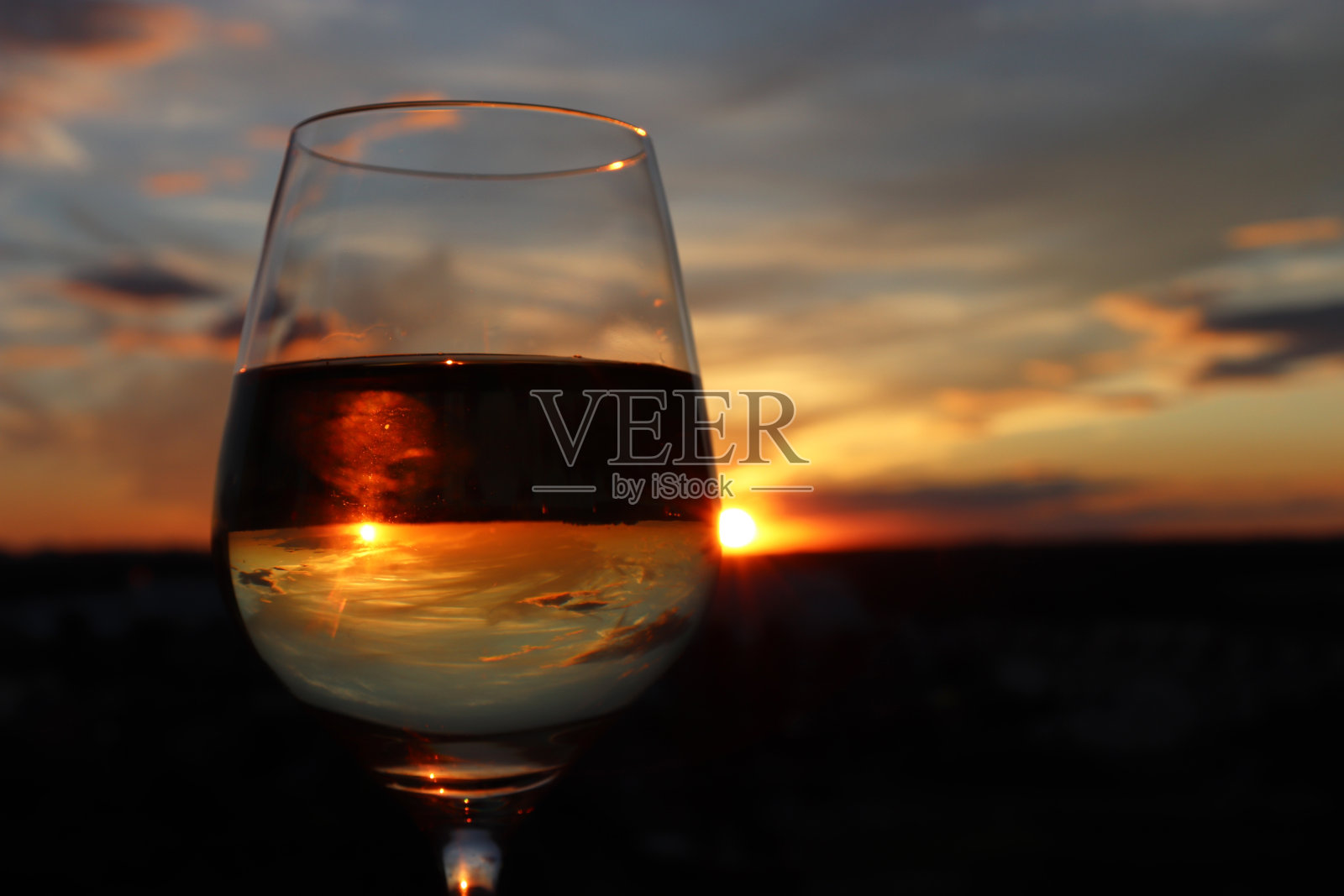 酒杯与白葡萄酒在美丽的日落背景，太阳和天空反映在酒精饮料照片摄影图片