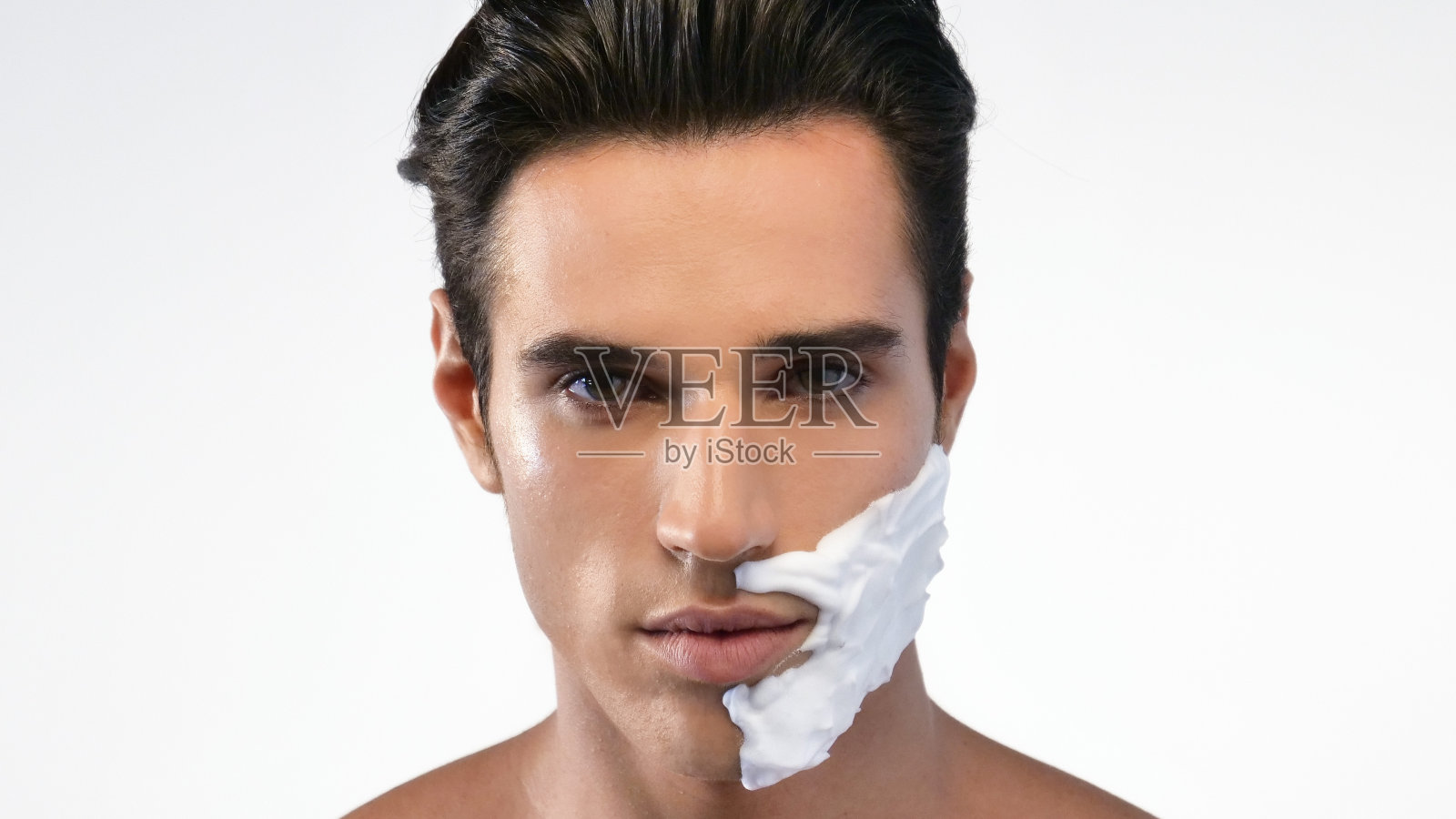 英俊的男人没有胡子，皮肤光滑无毛。半边脸抹了剃须泡沫刮得好一点，半边脸刮得好一点。照片摄影图片