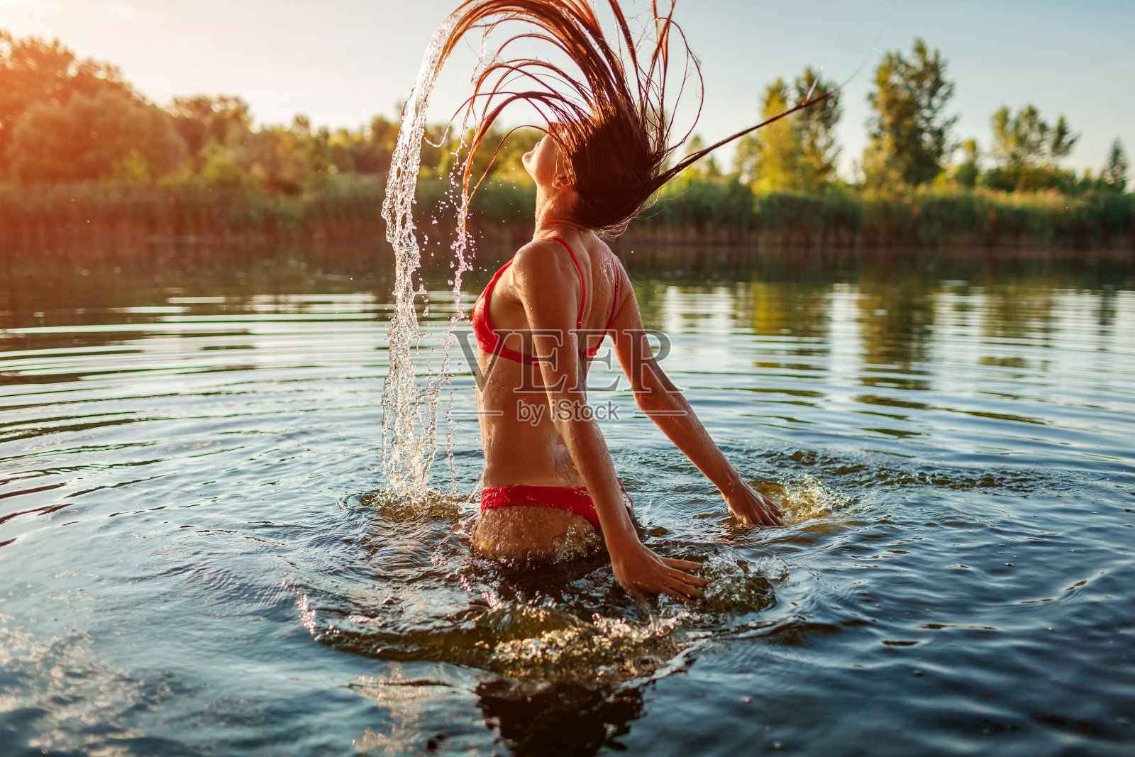 穿着比基尼的年轻女子在水里玩，溅起水花。暑假照片摄影图片
