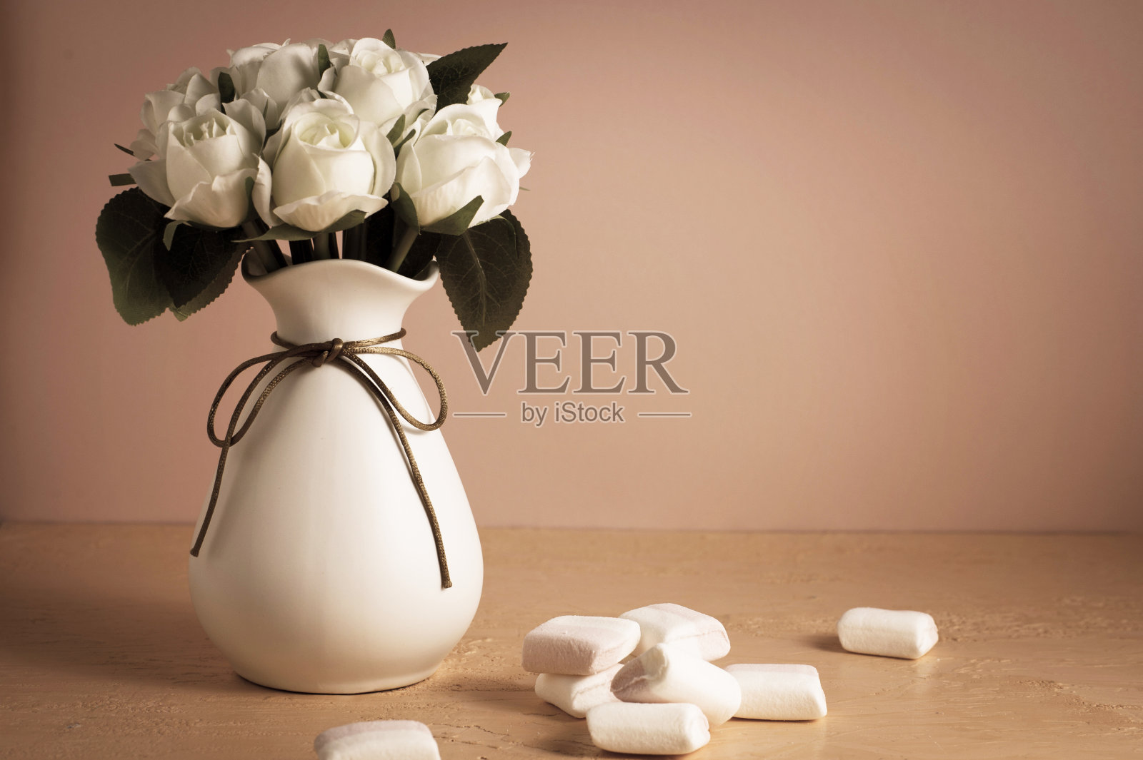 彩色的迷你棉花糖放在一张桌子上，旁边是粉红色背景上的白玫瑰。照片摄影图片