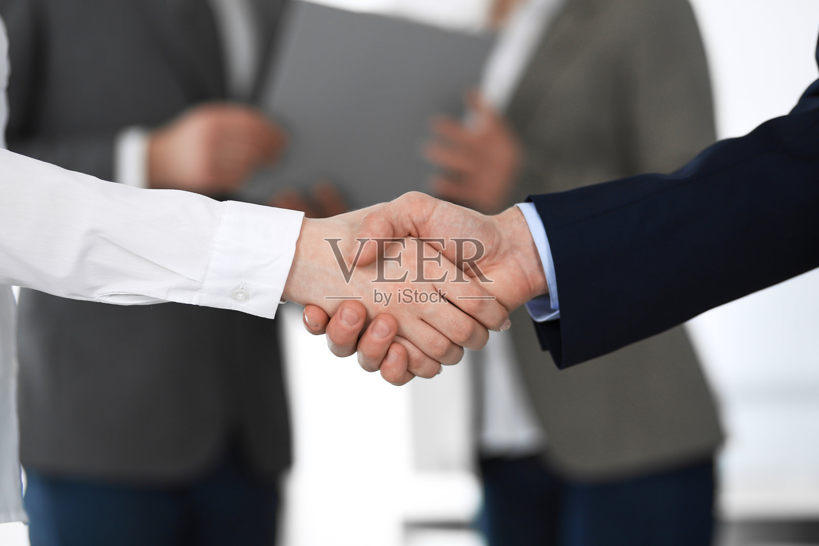 商务人士在会议或谈判中握手，特写。一群不知名的商人和女性在现代办公室的背景。团队合作，伙伴关系和握手的概念。照片摄影图片