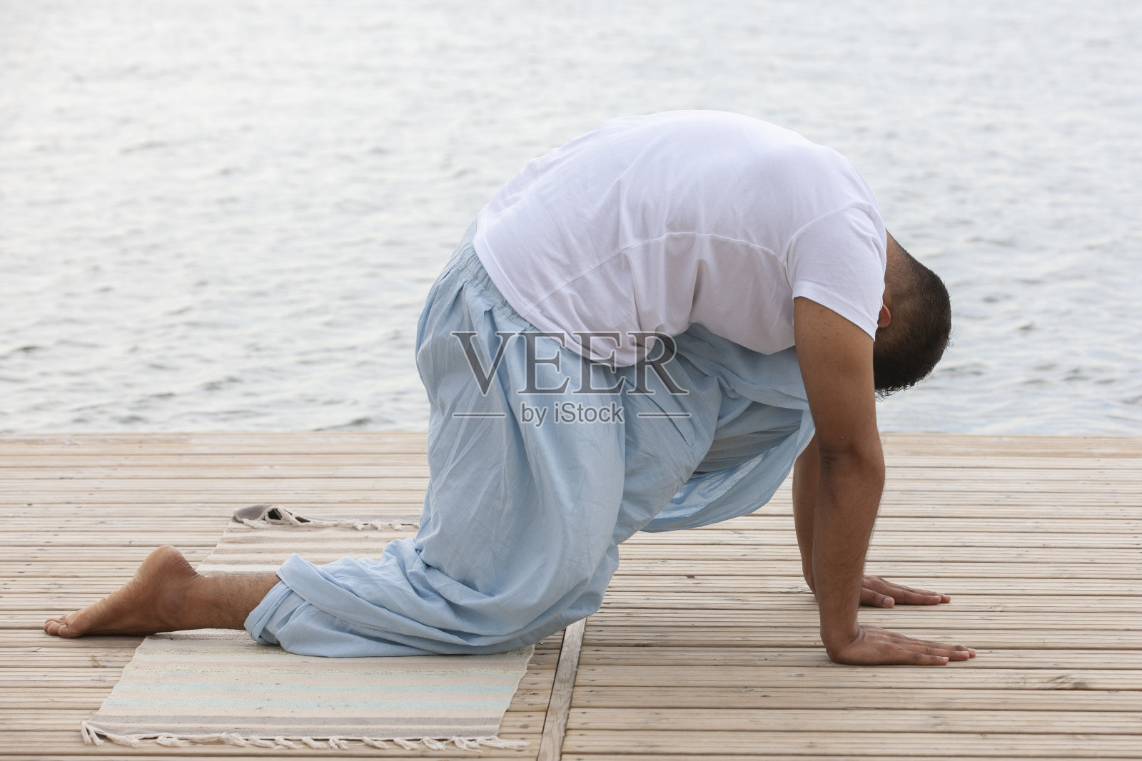 一个成熟的男人在湖边的码头上以莲花的姿势沉思照片摄影图片