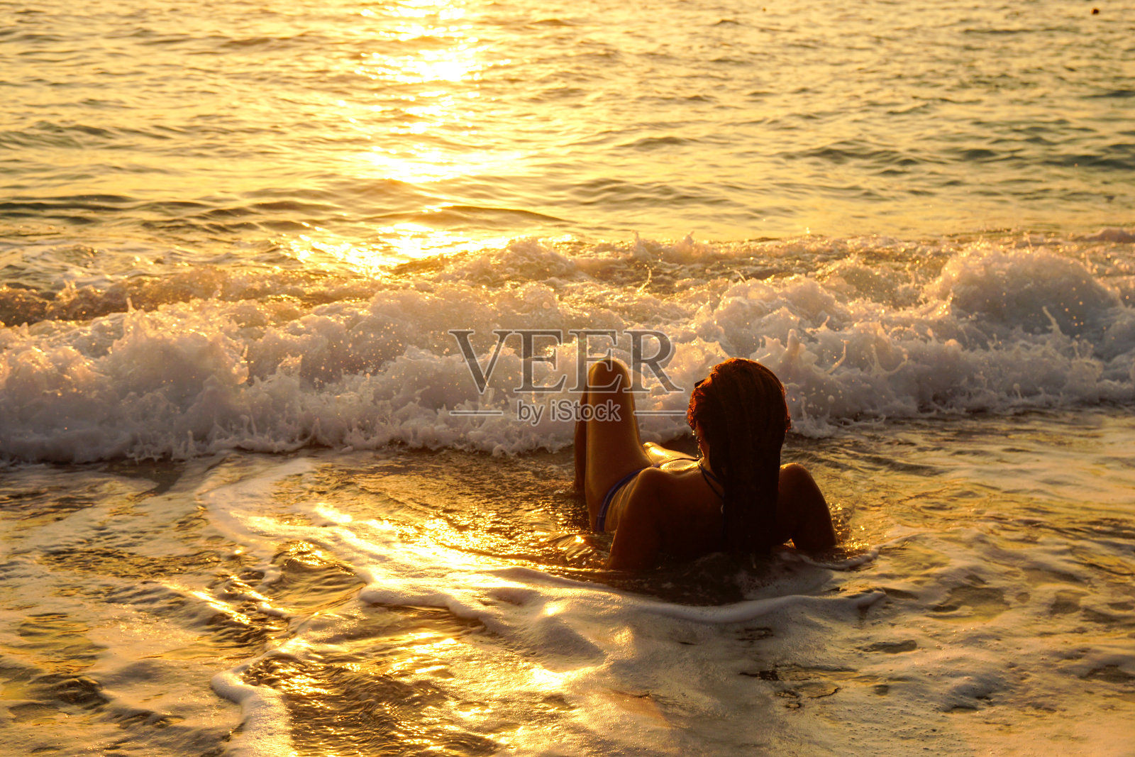 女人与波浪在日落的乐趣。照片摄影图片
