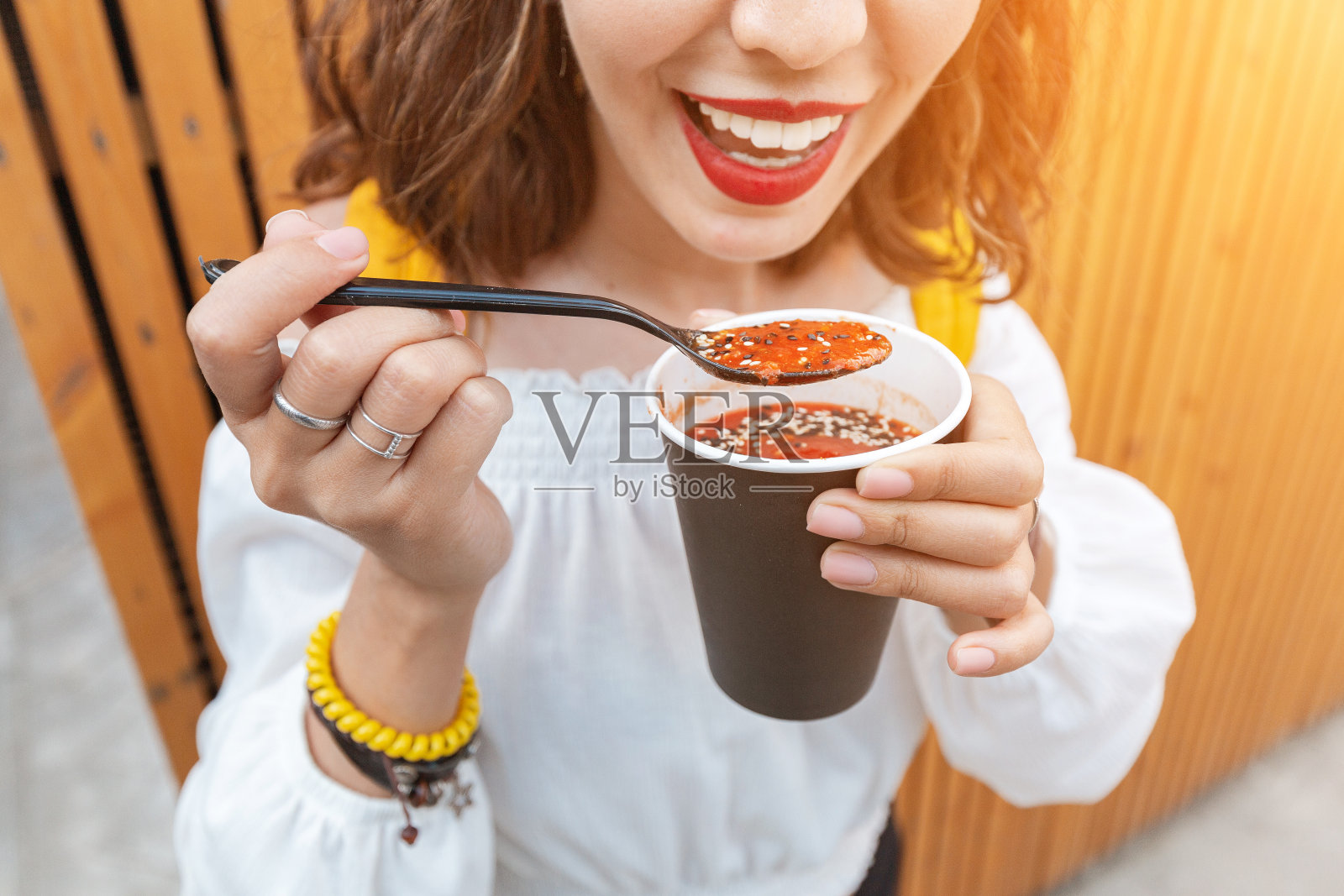 一个女人在街边吃着外卖纸杯里的素食西红柿汤。现代快餐的概念照片摄影图片