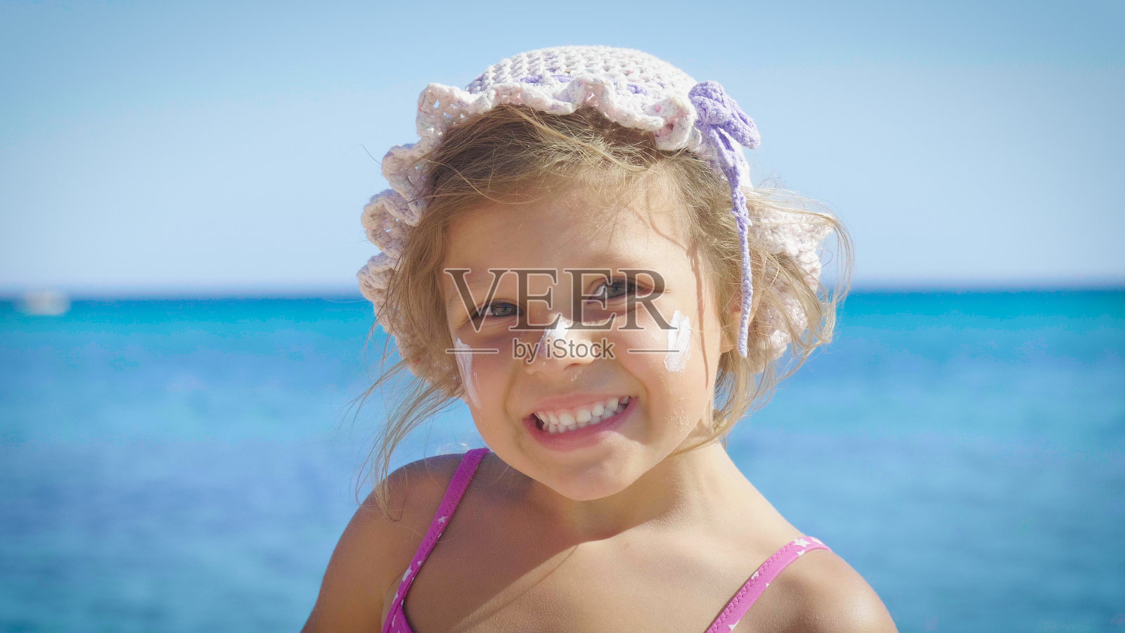 美丽可爱的小女孩的肖像是在海边玩可爱的微笑在巴拿马与太阳防护霜在海蓝色的水的背景。照片摄影图片