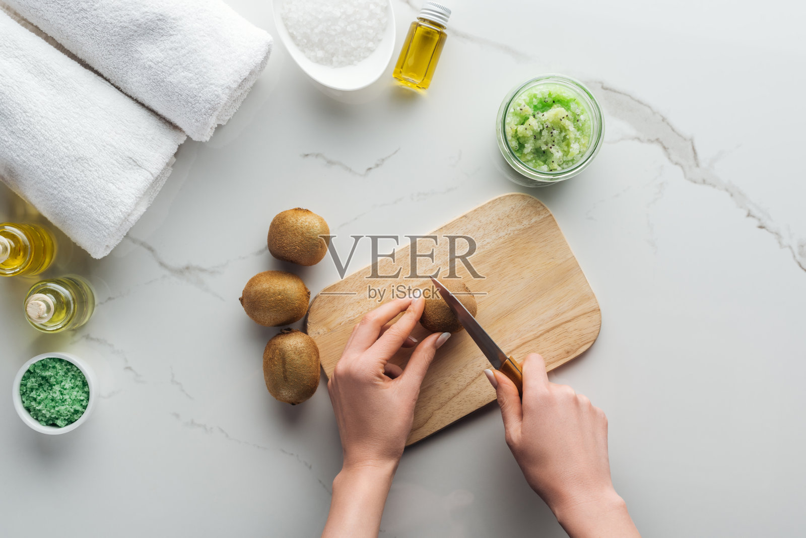 女性在木质切割桌上切割猕猴桃，白色表面上手工制作化妆品的各种天然成分照片摄影图片