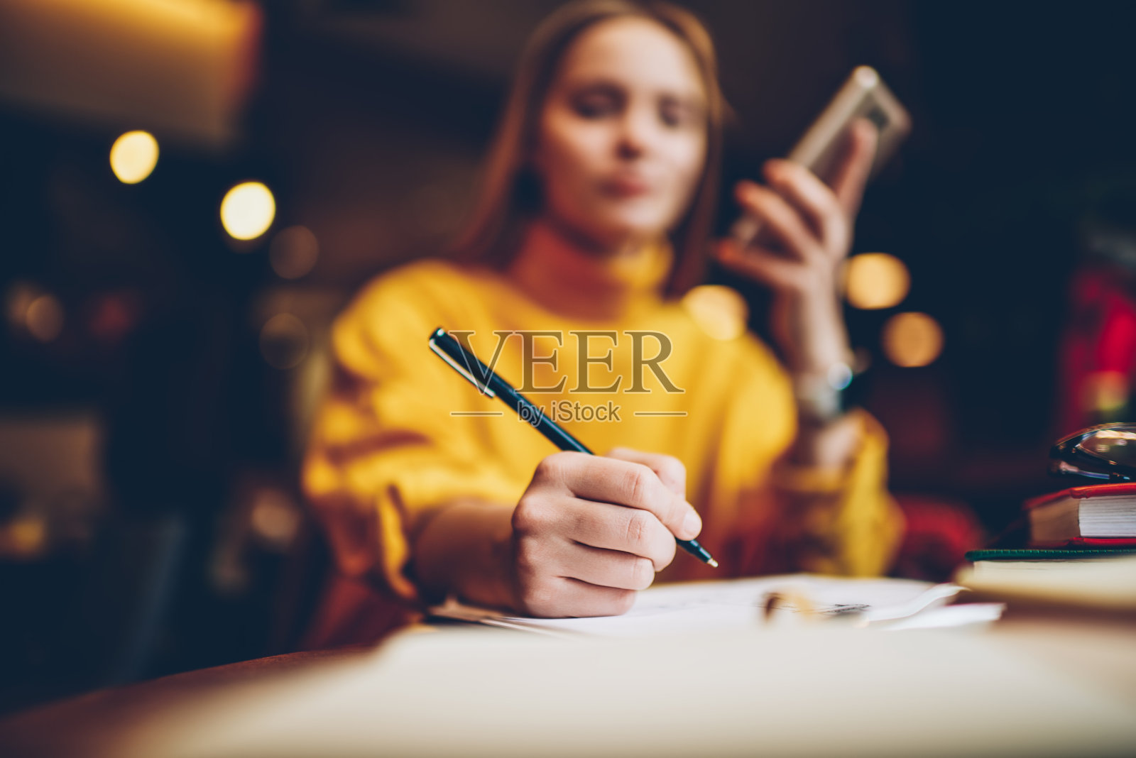 在咖啡厅工作时，有选择的专注于女人的手握笔，将一些信息写在记事本上。模糊形象的智能女学生准备即将到来的考试室内照片摄影图片