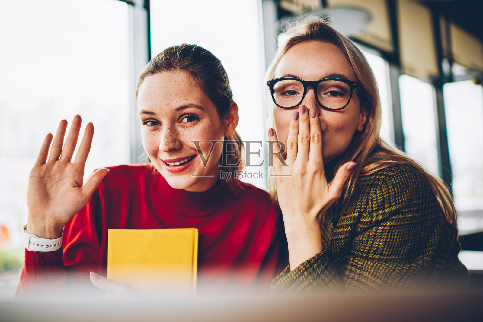 半长肖像的快乐的年轻女子挥手和金发潮学生与飞吻微笑的镜头。快乐漂亮的博主与情感表达花自由时间在一起照片摄影图片
