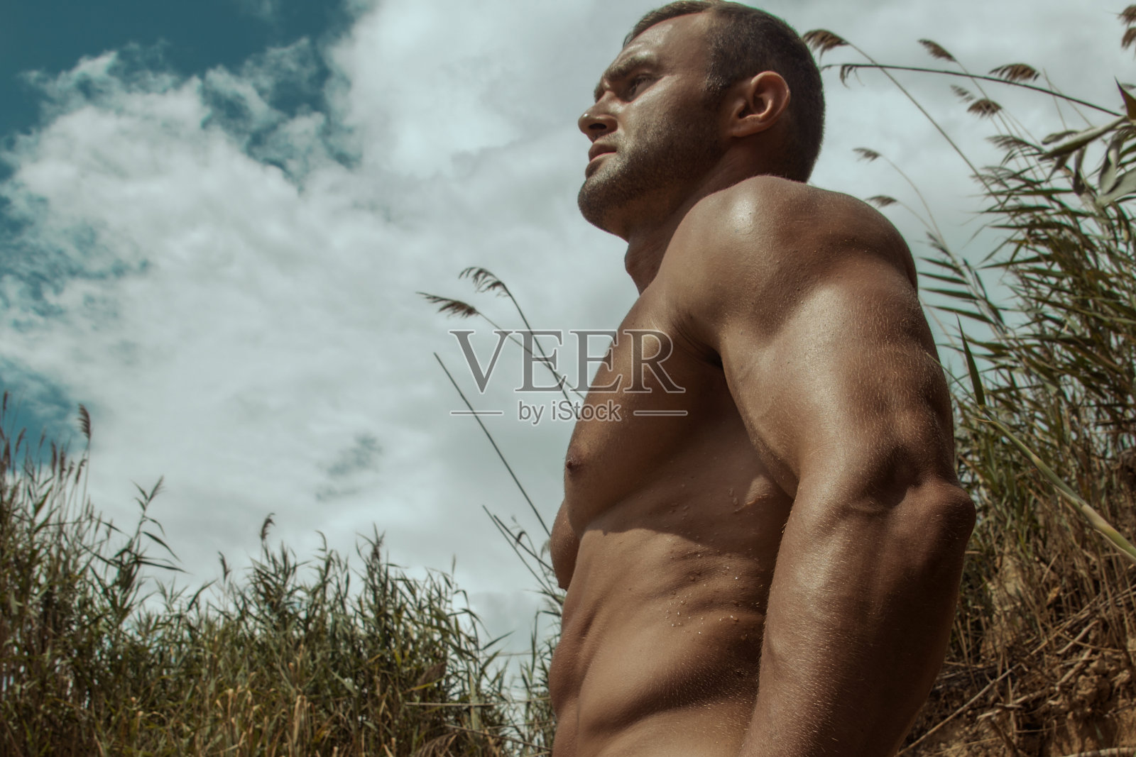 性感的运动肌肉美丽的条纹男模特与白色的毛巾和泳衣在自然的背景与大海和岩石，沙子和天空在海滩上的日落照片摄影图片