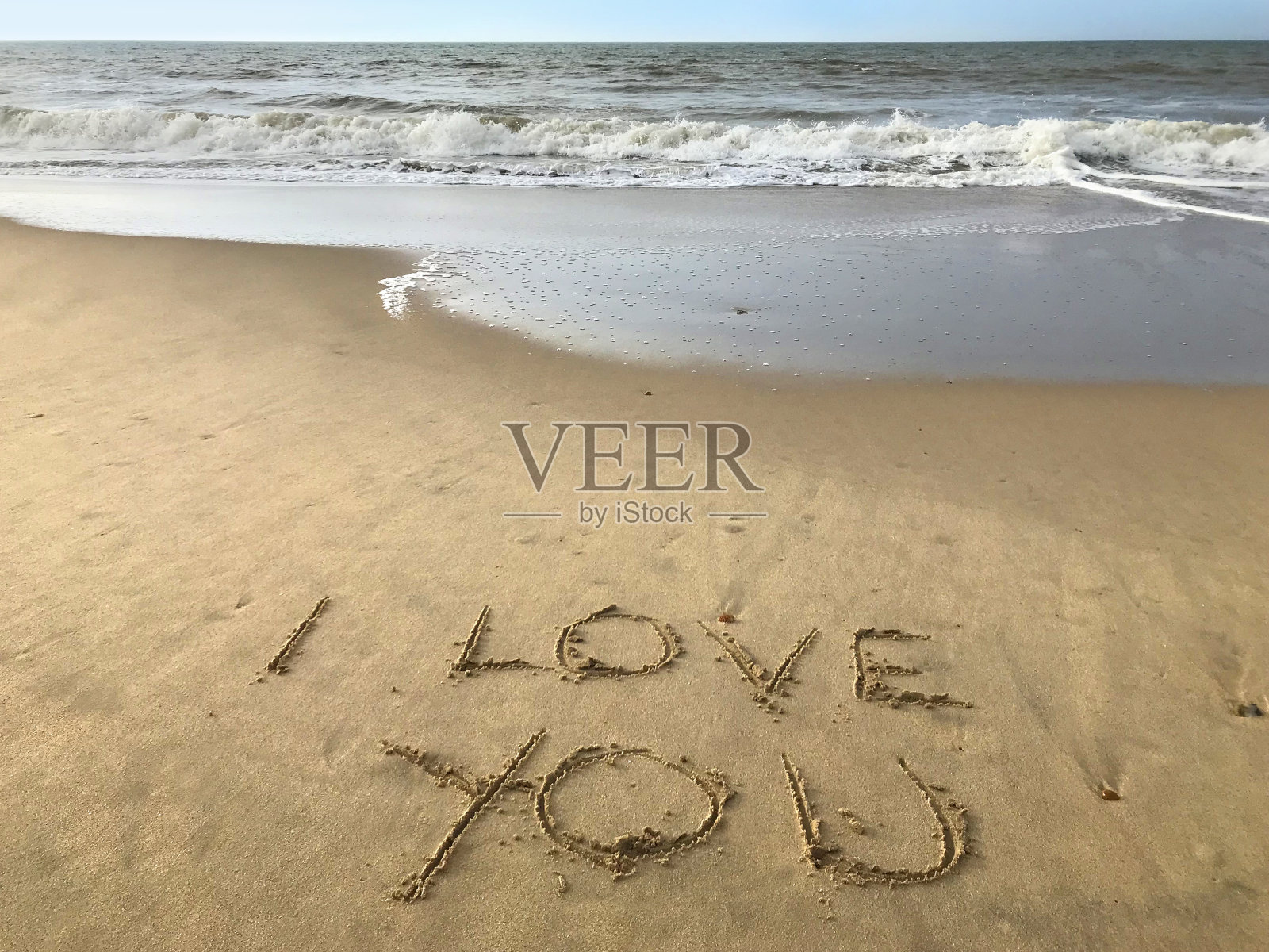 在阳光明媚的海滩上写下我爱你的话，用棍子写在沙子上，由海浪，概念社交媒体照片在柔软的金色沙滩上书写字母，多塞特，英国海边海岸线的景色照片摄影图片
