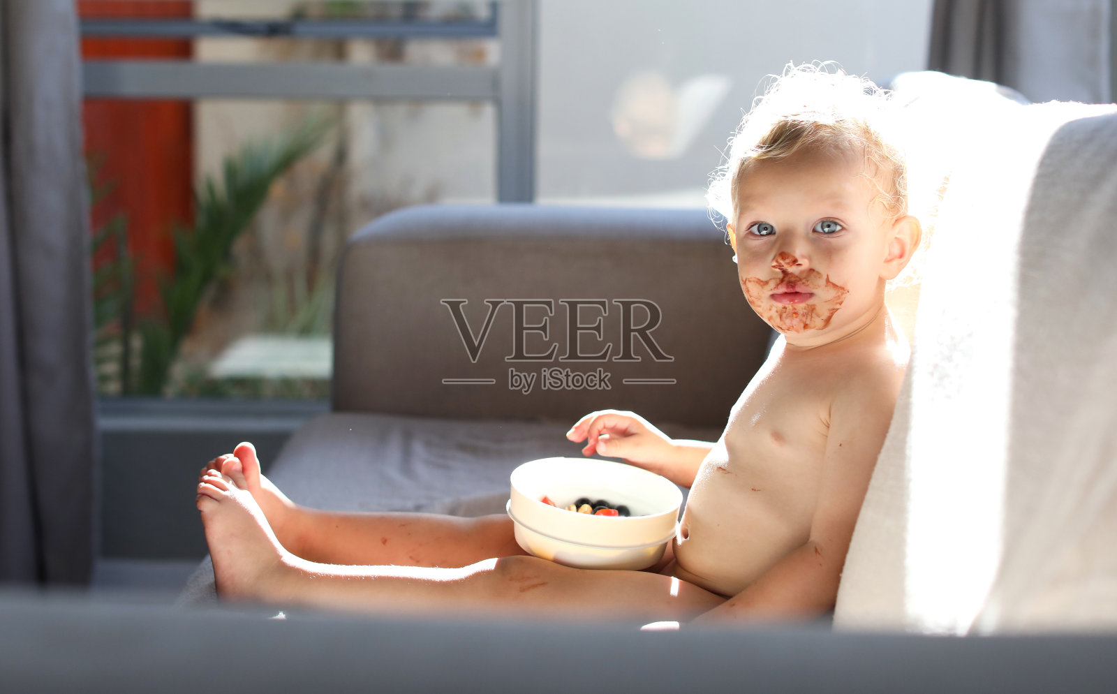 一个脸上沾着巧克力的小孩在沙发上吃零食。照片摄影图片