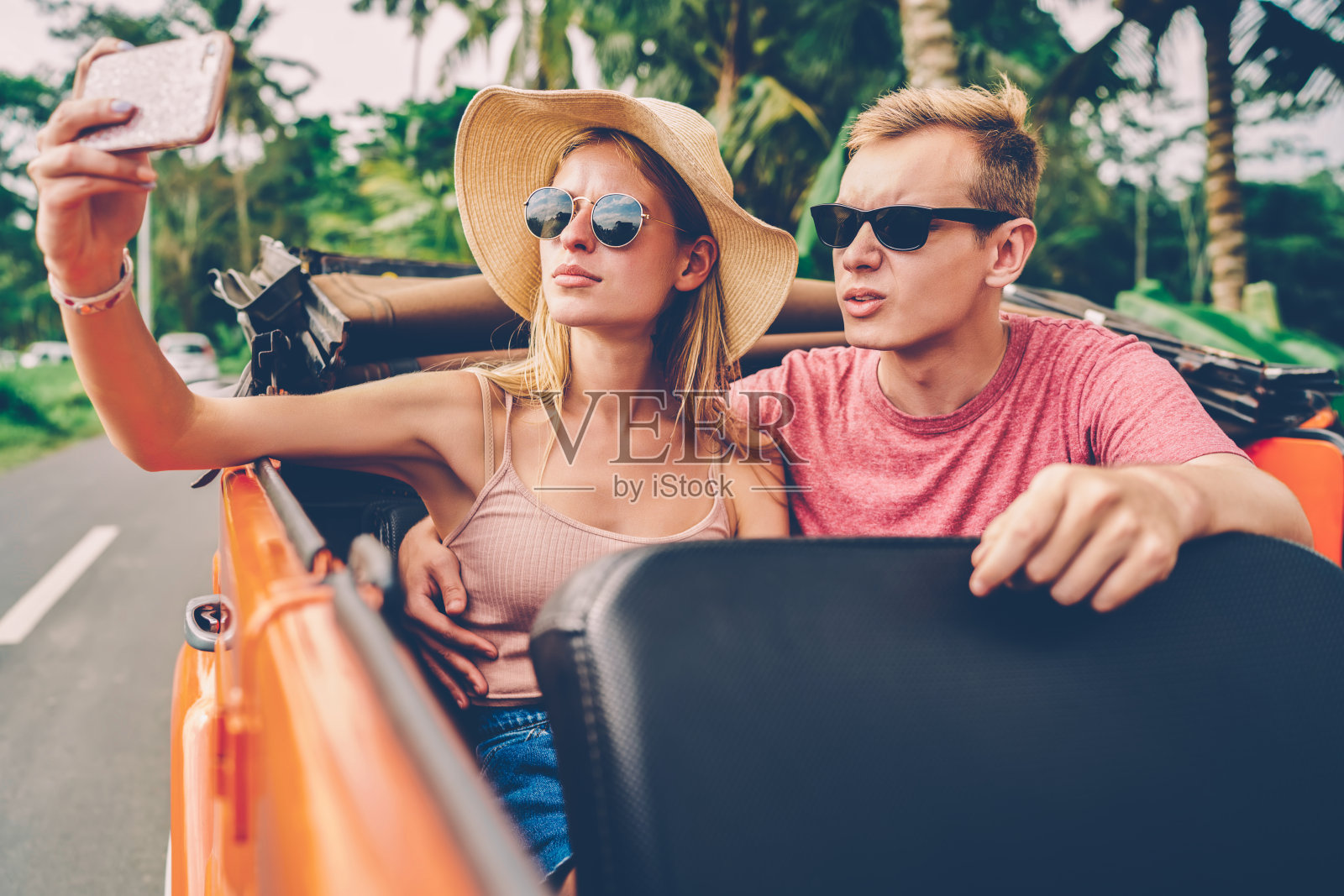 时髦的女孩戴着墨镜用智能手机拍照，和男友自拍分享到网络上，相爱的情侣在公路上租了一辆车，在手机上摆姿势拍摄共同的照片照片摄影图片