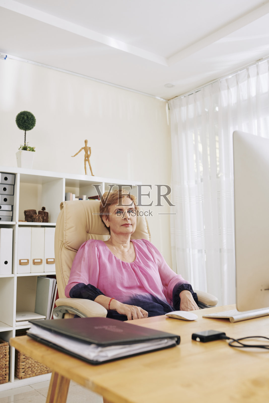 坐在她办公室桌子旁的资深女性照片摄影图片