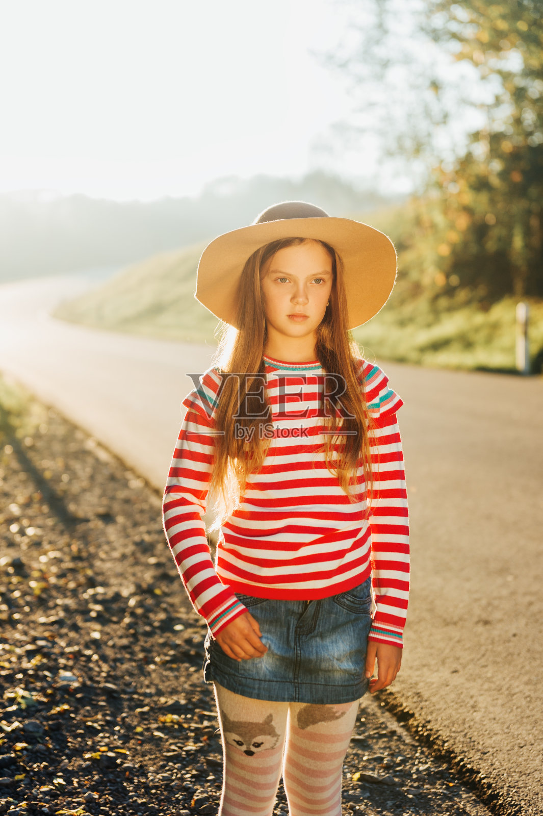 户外肖像的漂亮女孩戴着大帽子，粉红色条纹套衫和牛仔裙照片摄影图片