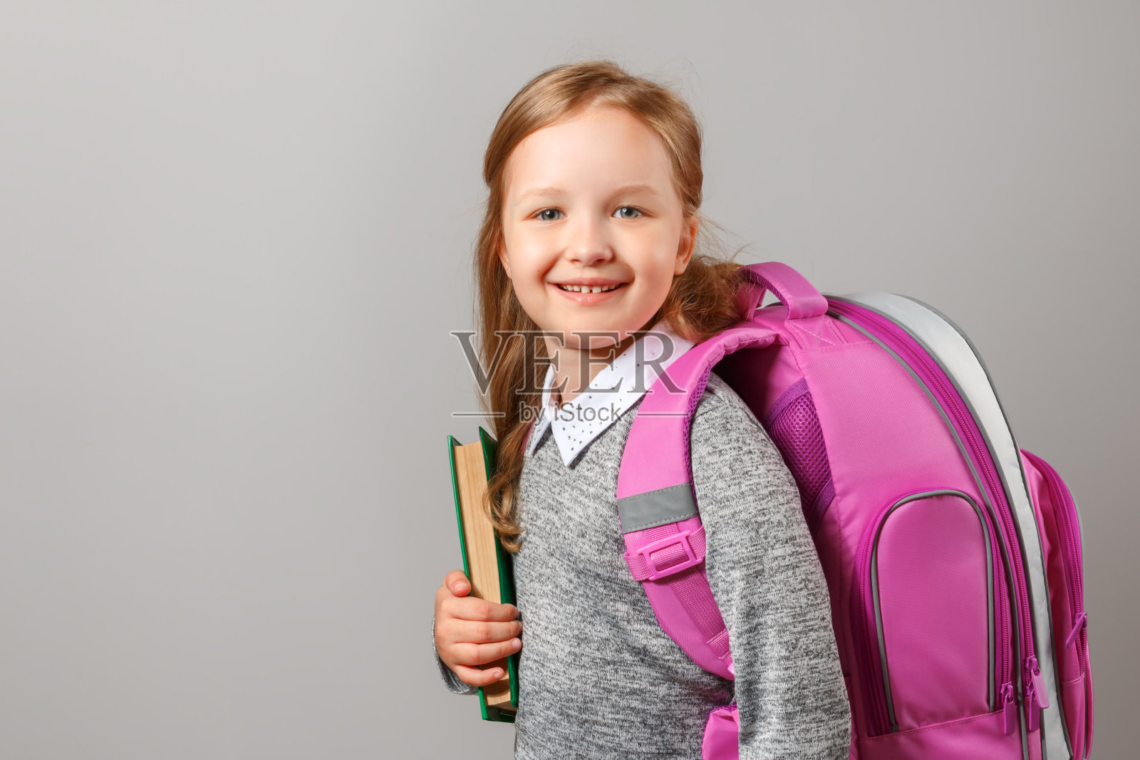 小女孩的肖像与书包和书在灰色的背景。迷人的孩子学生特写。回到学校。教育观念。照片摄影图片