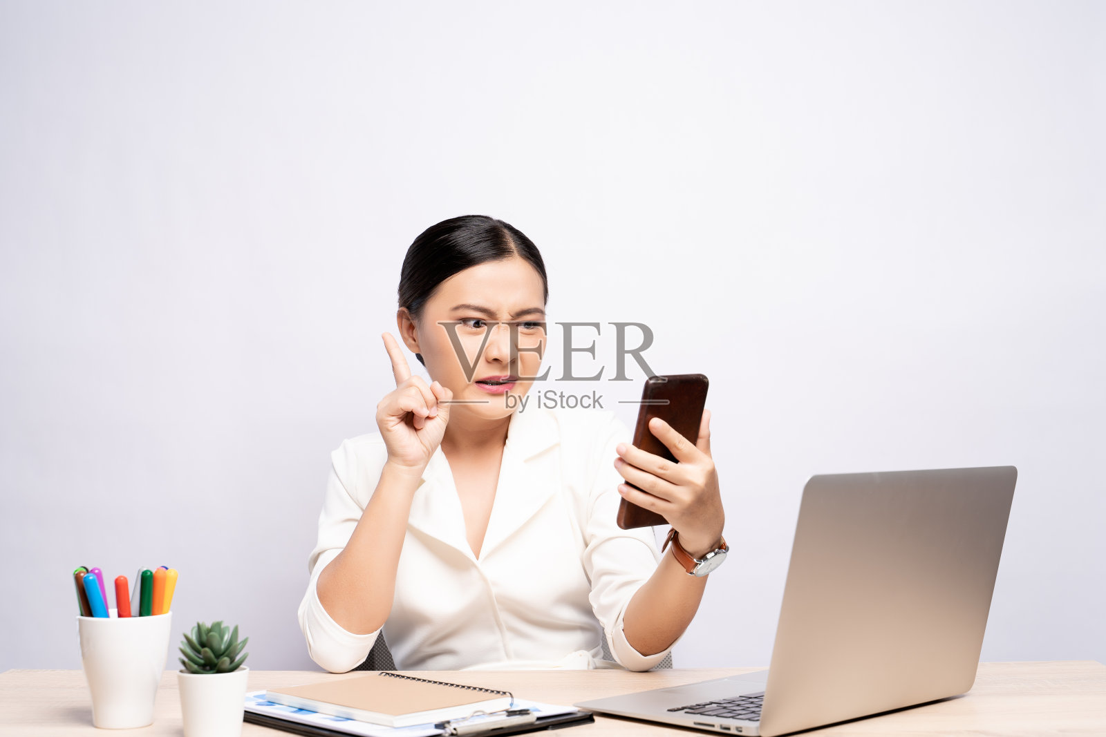 女人看智能手机，在办公室孤立的背景下做出八卦手势照片摄影图片