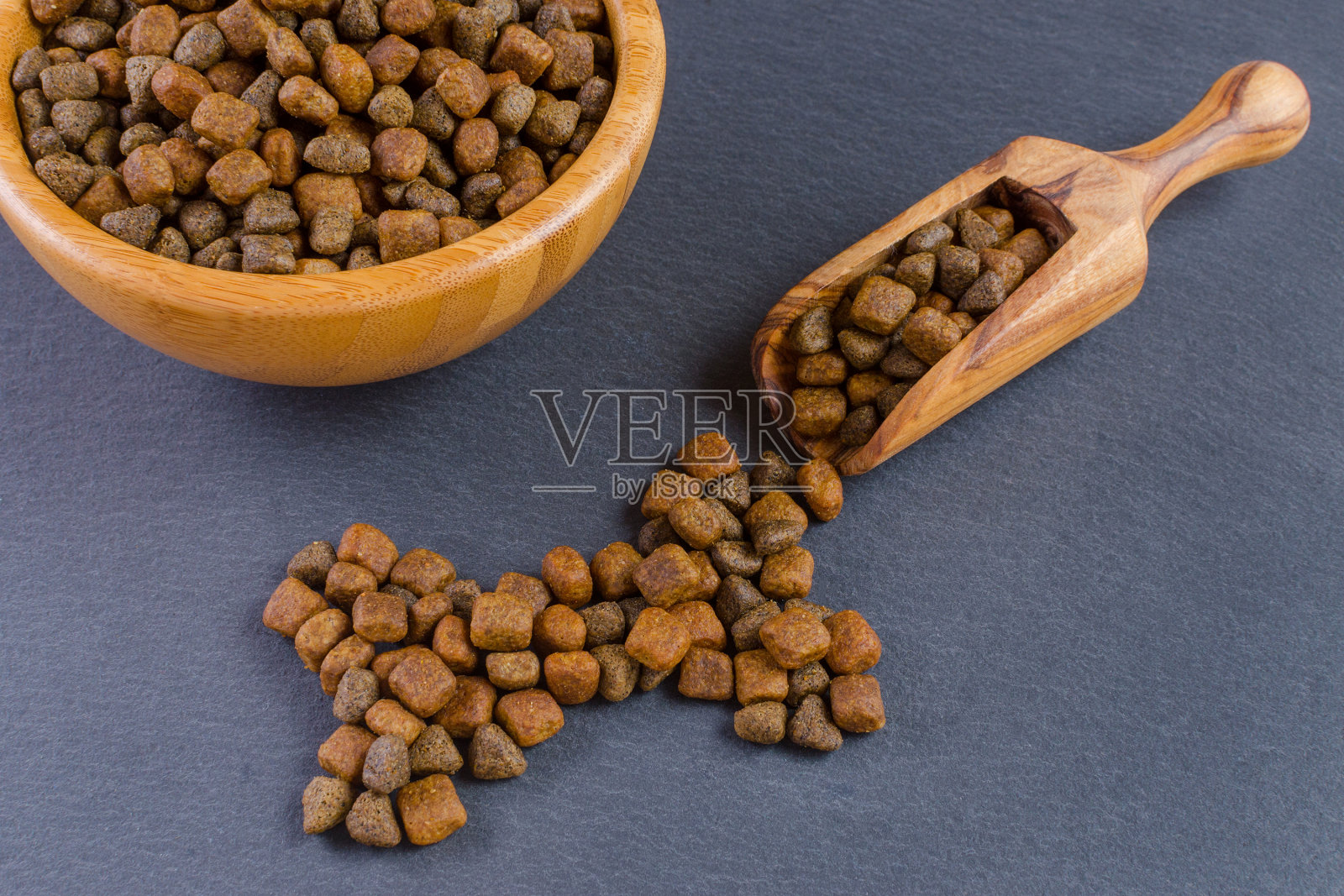 狗粮装在木碗里，黑色背景上有一个勺子照片摄影图片