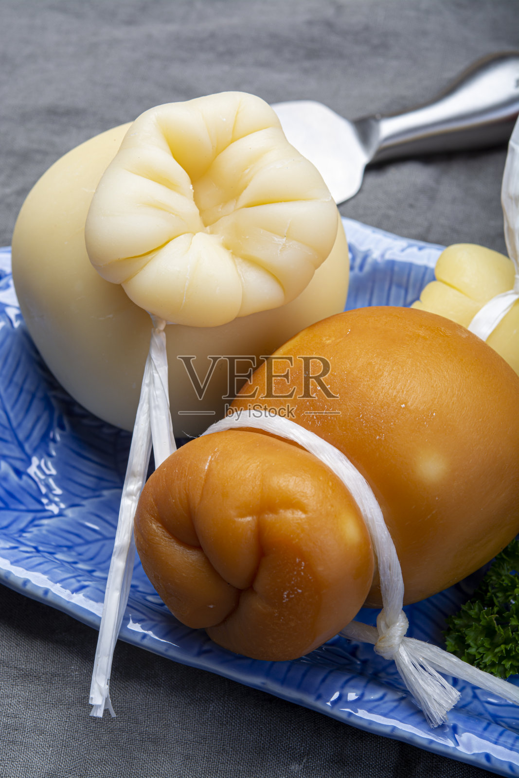 意大利波萝伏洛干酪泪滴状的陈年烟熏奶酪，放在靠近的蓝色盘子里照片摄影图片