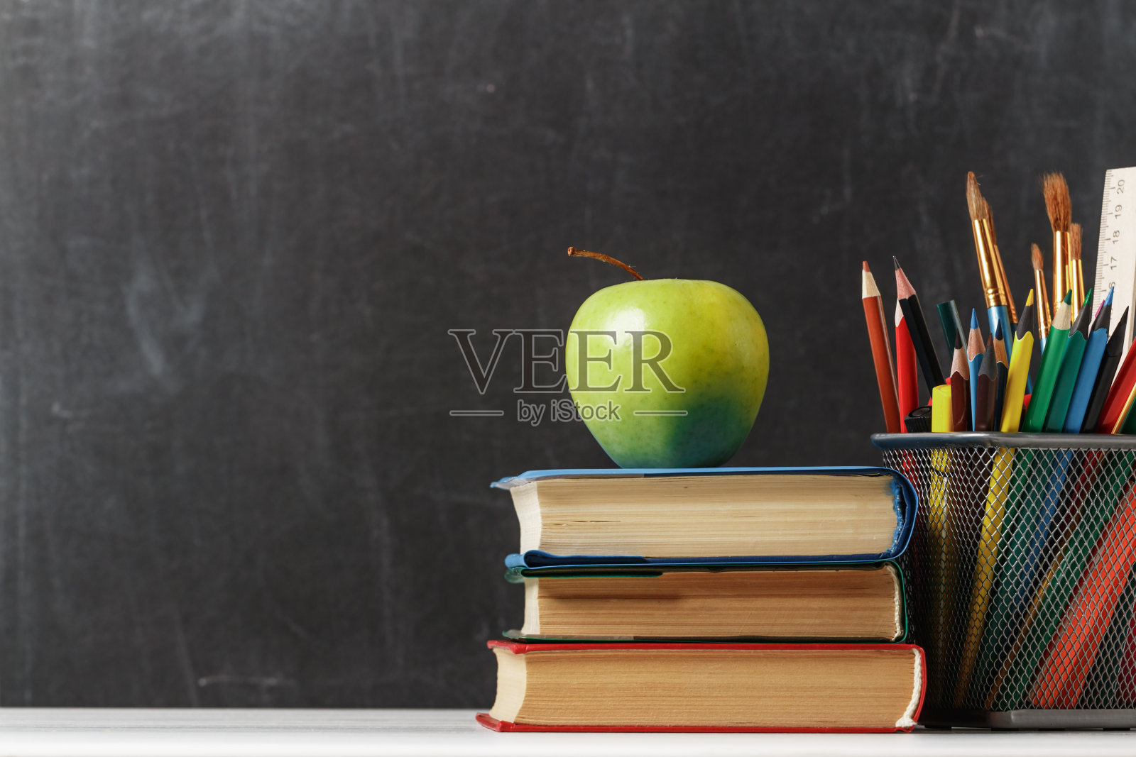 为学生设置。一堆书，一个苹果，铅笔，背景是学校的黑板。教育观念。本空间照片摄影图片