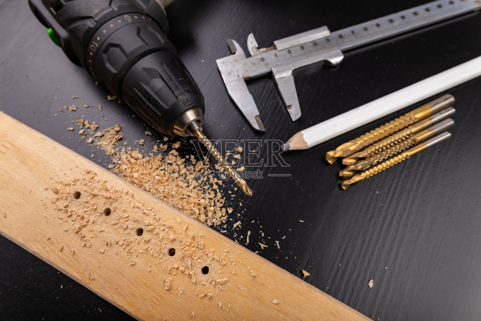 在一块刨过的干木头上钻孔。用螺丝刀在车间打洞。黑暗的背景。照片摄影图片